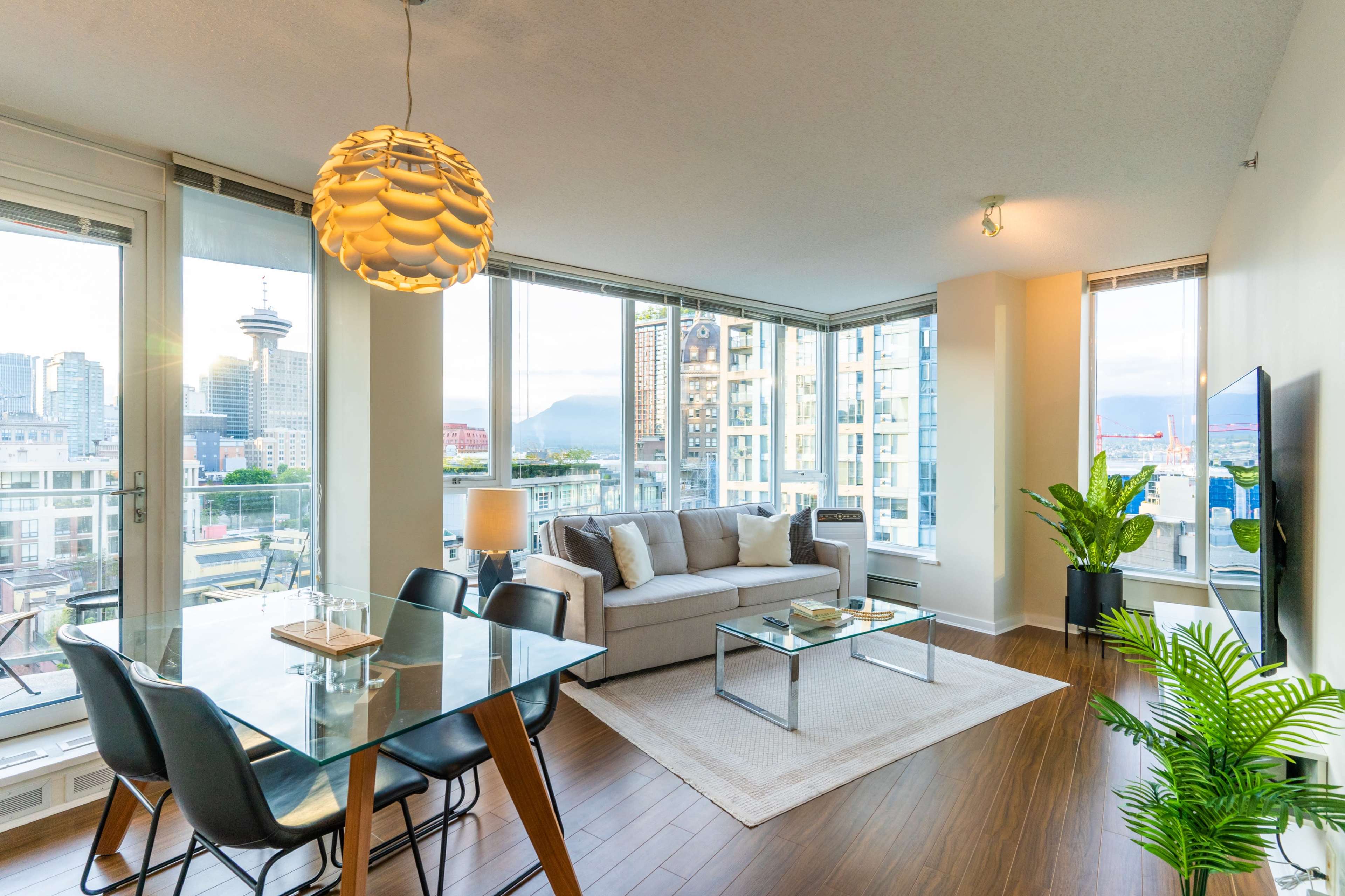 A modern living room and dining area feature large windows with city views, a sofa, a dining table, and a decorative plant.