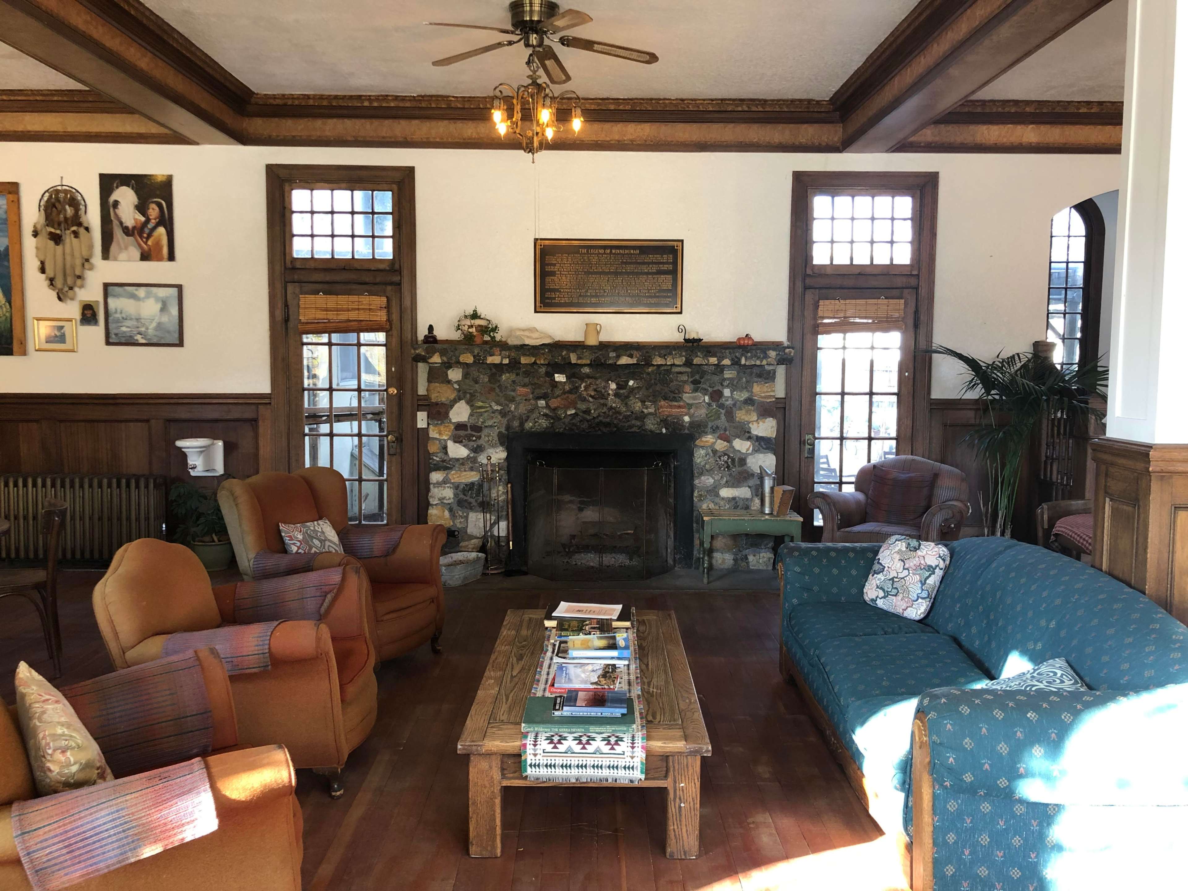 The living room features a stone fireplace surrounded by wooden walls, with various seating options, including two armchairs and a couch, arranged around a central coffee table.
