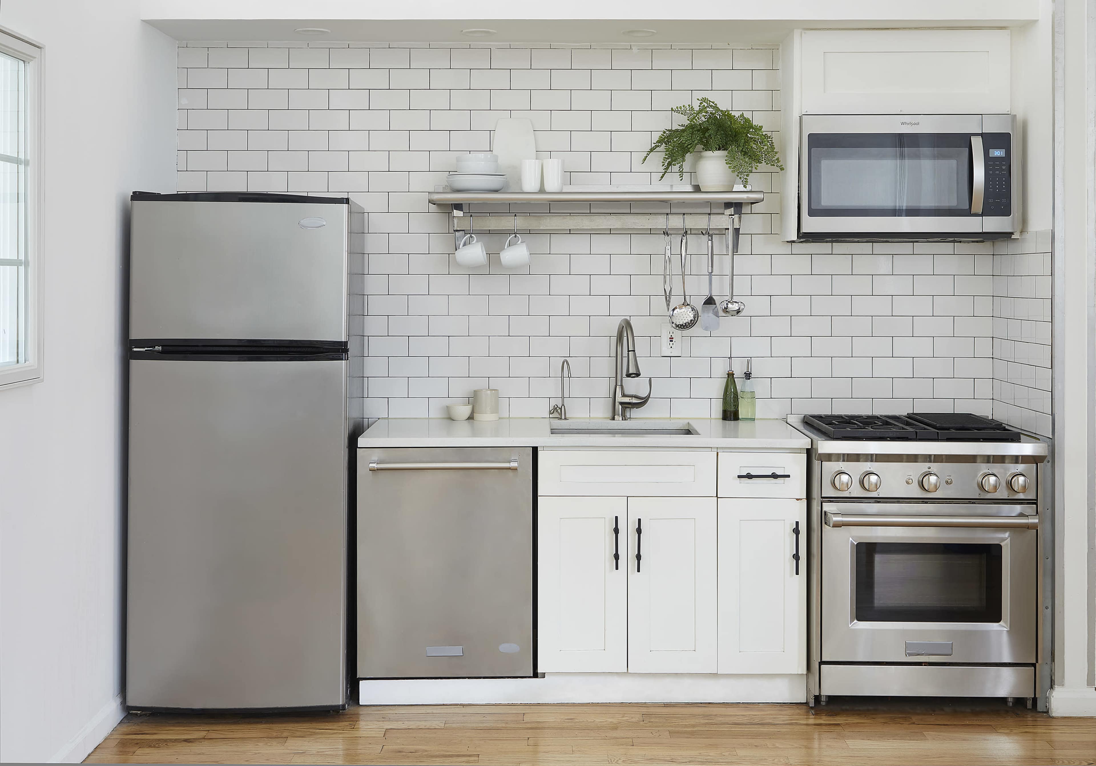 The image shows a modern kitchen with stainless steel appliances, including a refrigerator, dishwasher, and range, set against a white tiled backsplash.