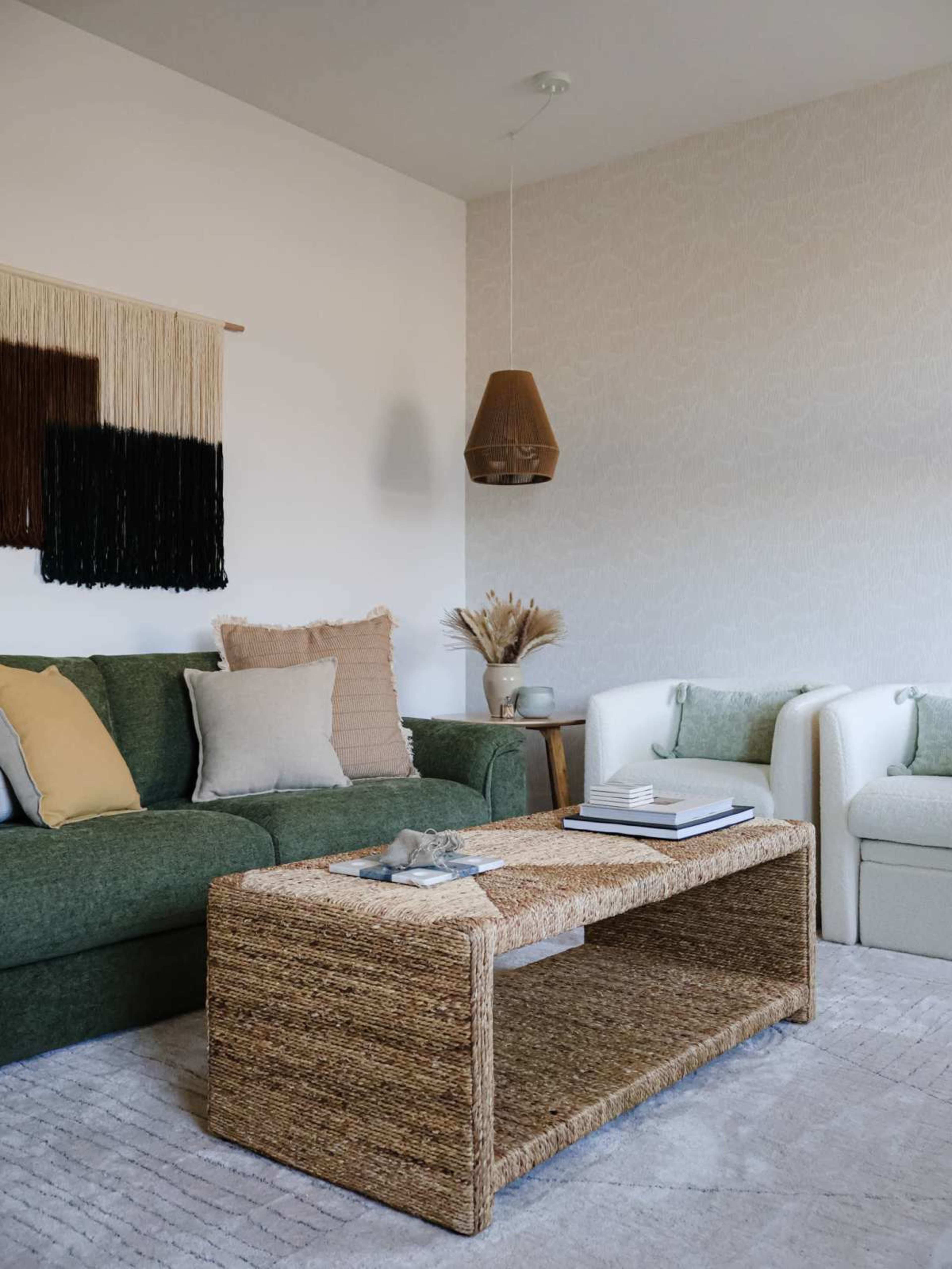 A living room features a green sofa, white armchairs, a woven coffee table, and decorative wall hangings.