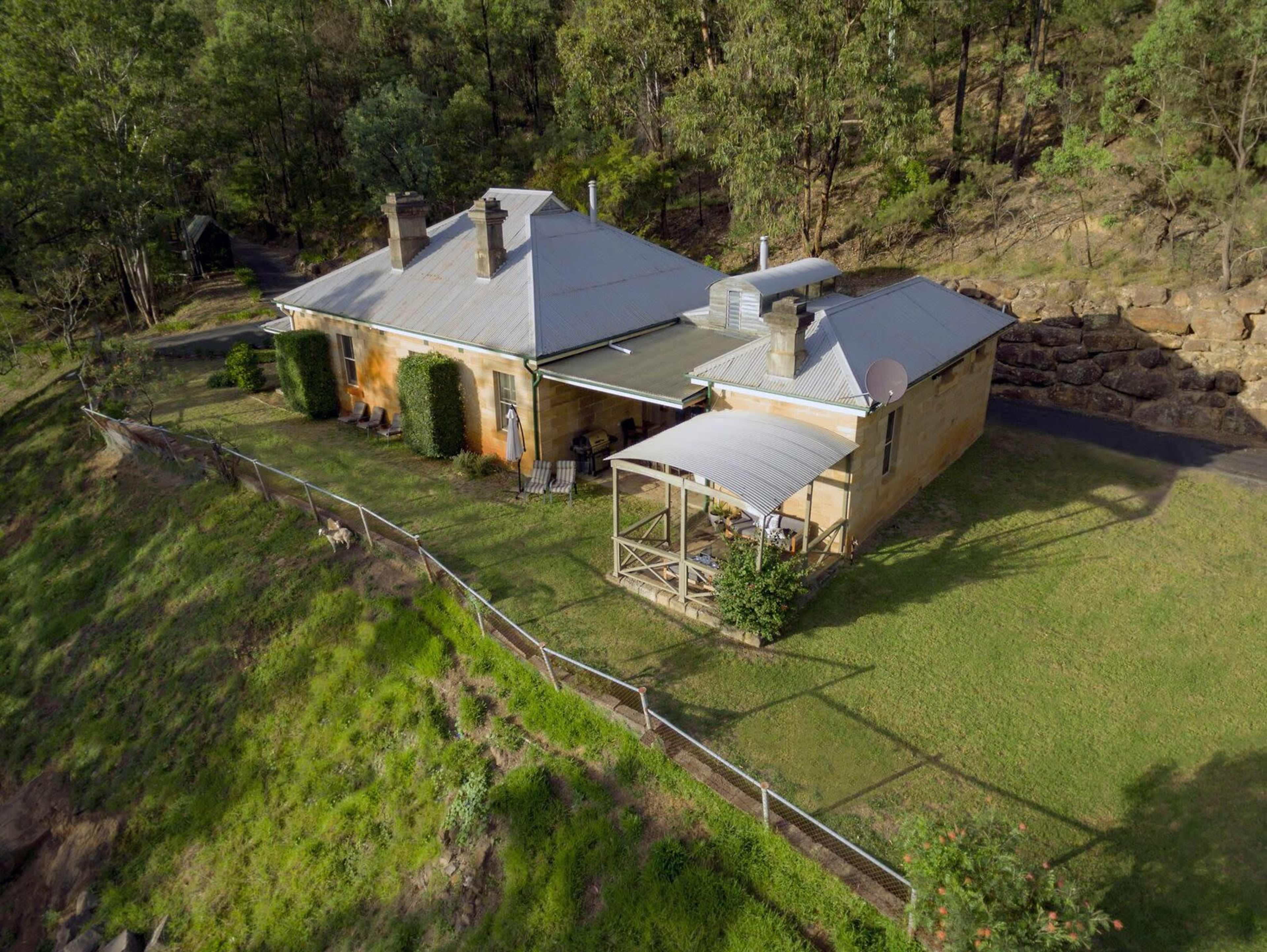 Aerial view of a stone house with a large lawn surrounded by trees and a gravel path.