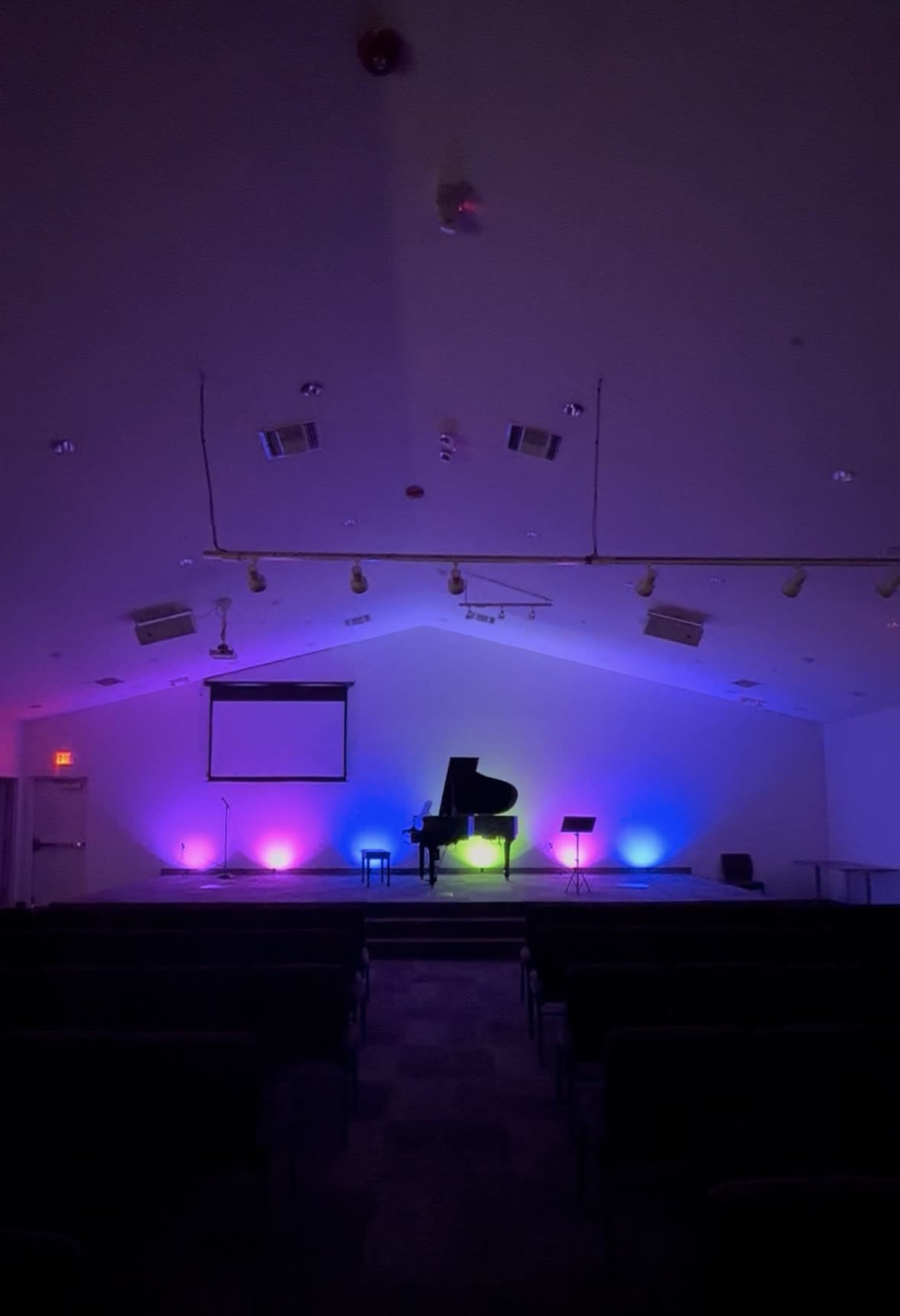 The image shows a dimly lit room with a grand piano on a stage, illuminated by colorful lights.