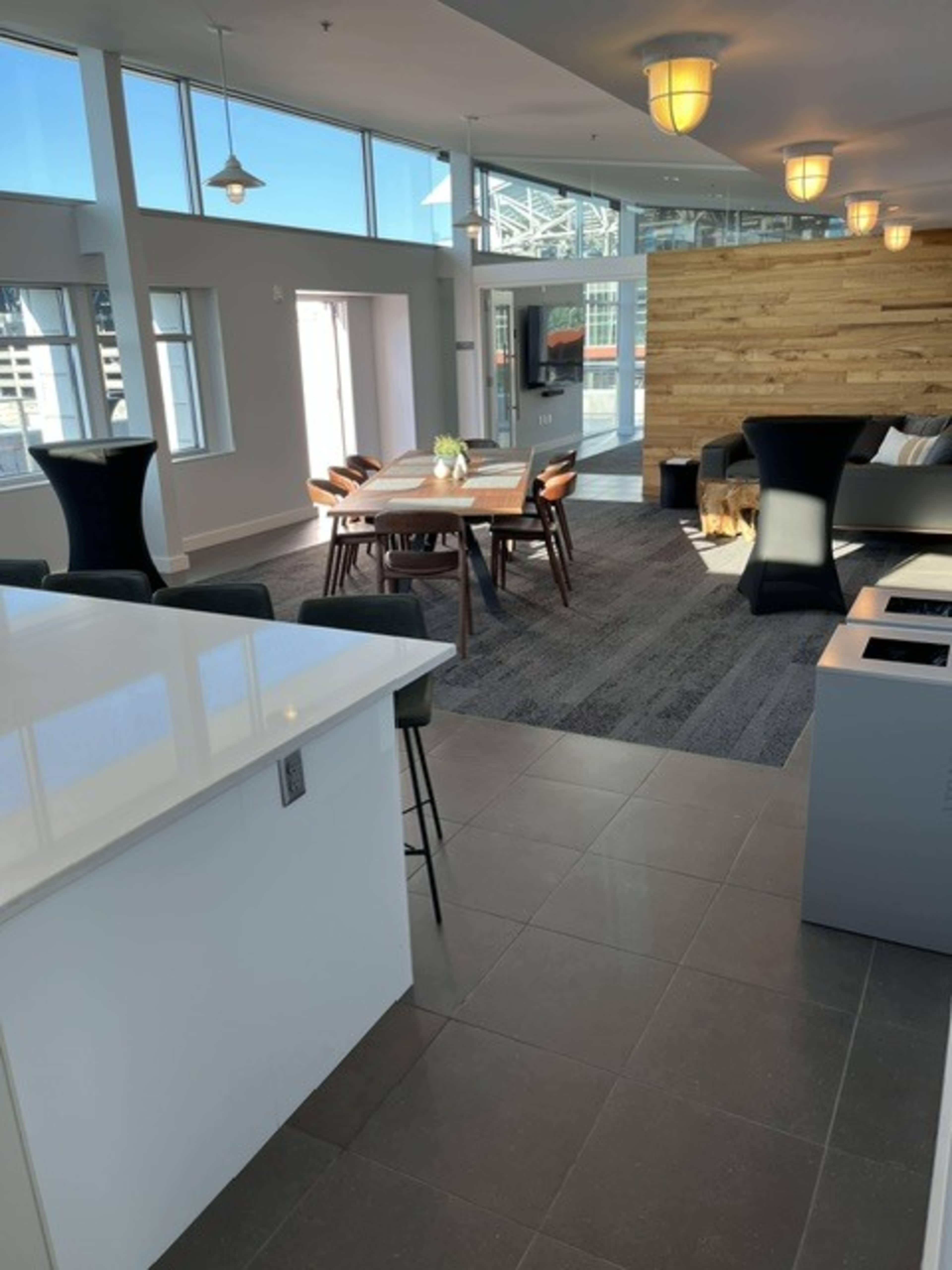 The image shows a modern, open-concept living space featuring a kitchen island, dining table, seating area, and large windows with a view.