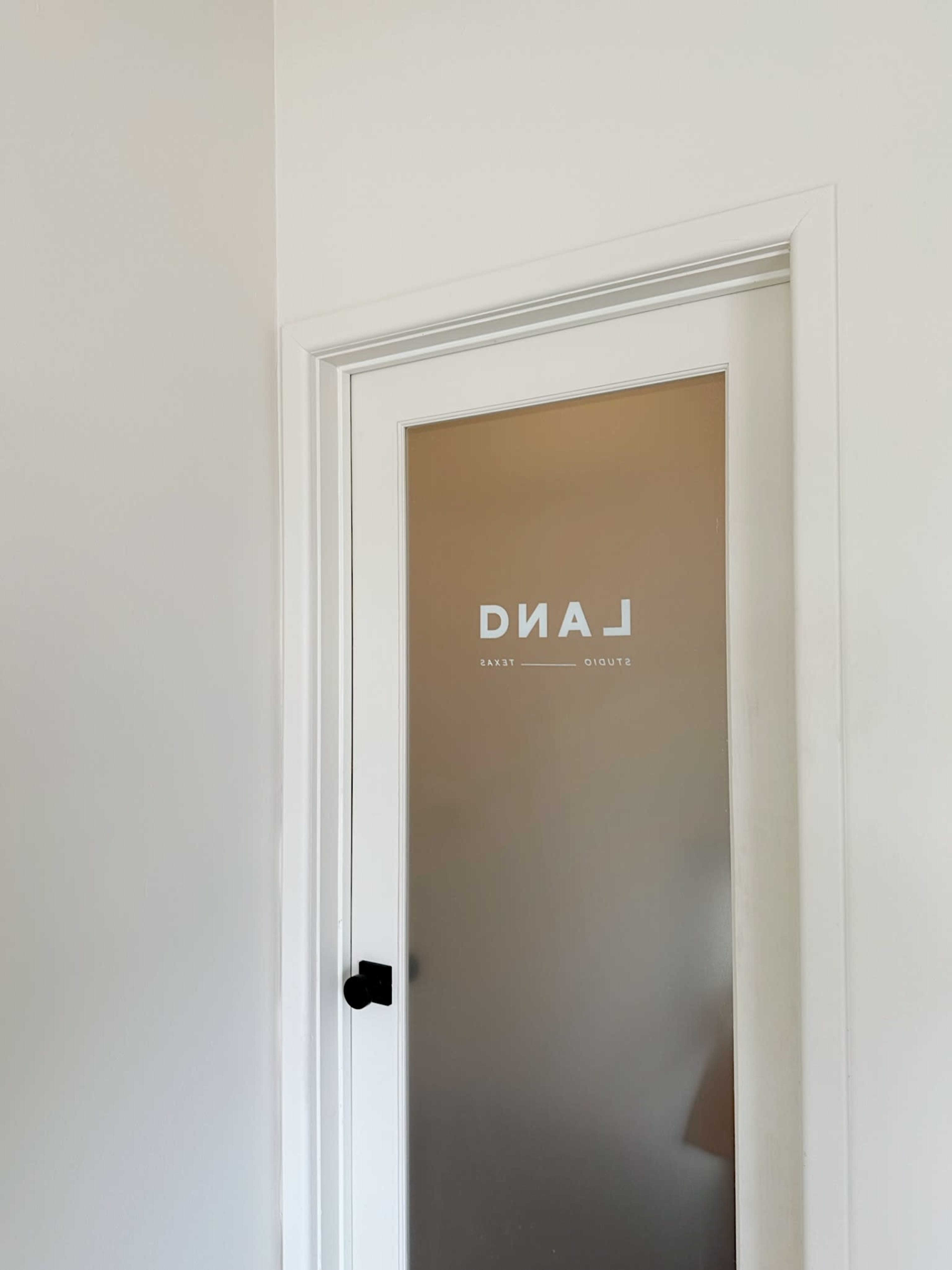 The image shows a frosted glass door with the word "LAND" printed on it, set within a white wall.