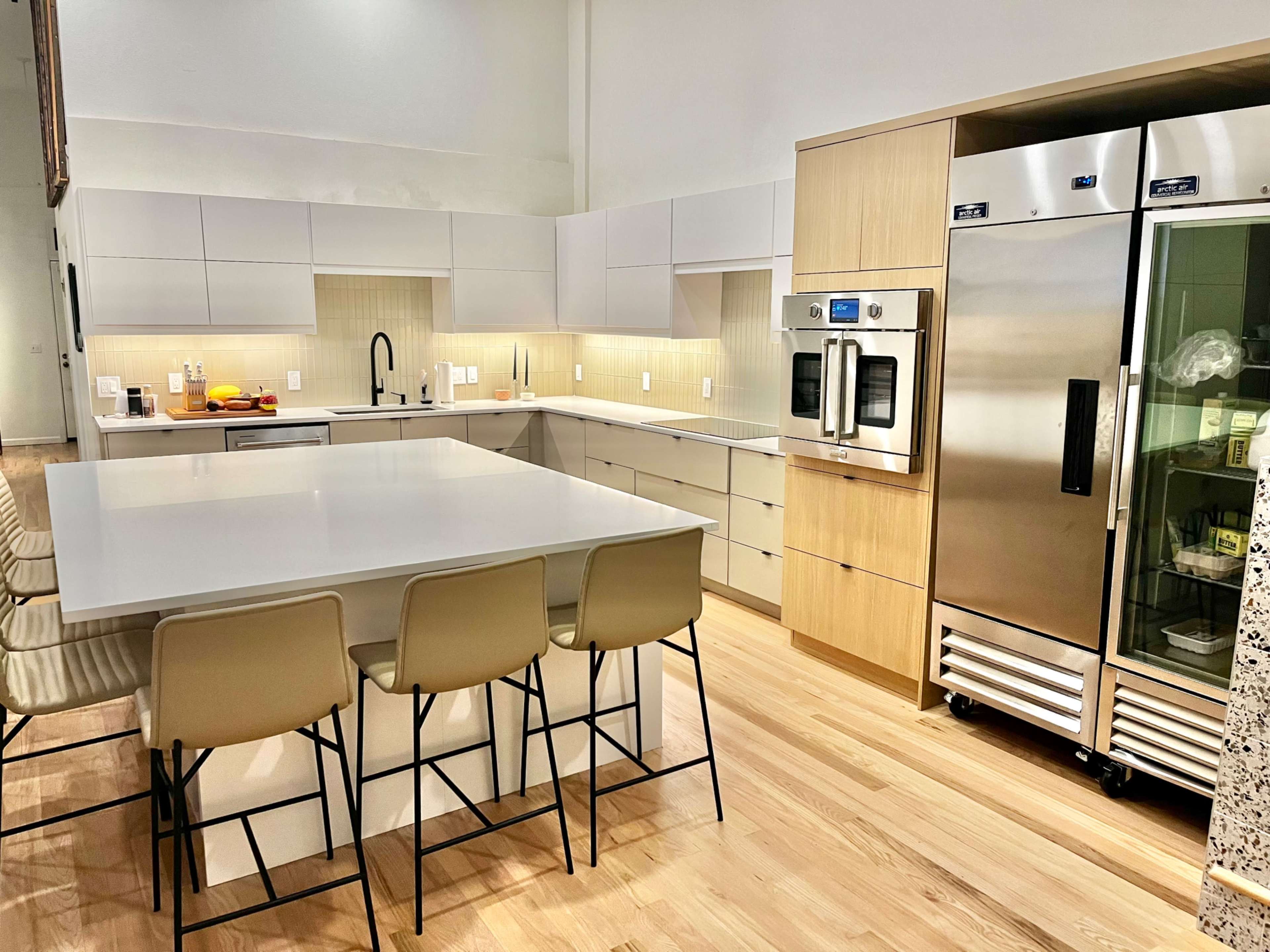 A modern kitchen features a large central island with bar stools, sleek cabinetry, and stainless steel appliances.