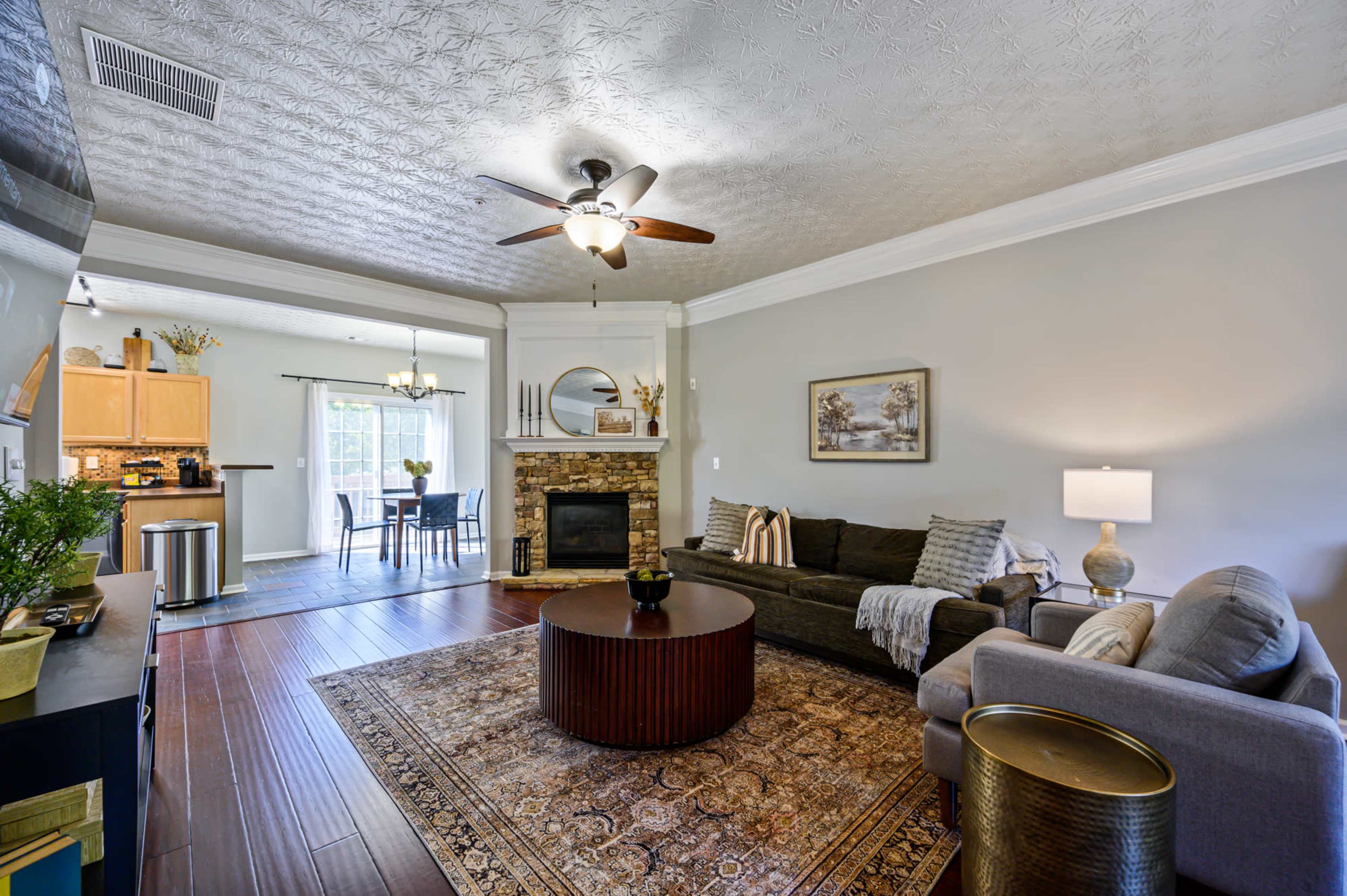 A living room with a stone fireplace, a circular coffee table, a sofa, and a dining area visible in the background.