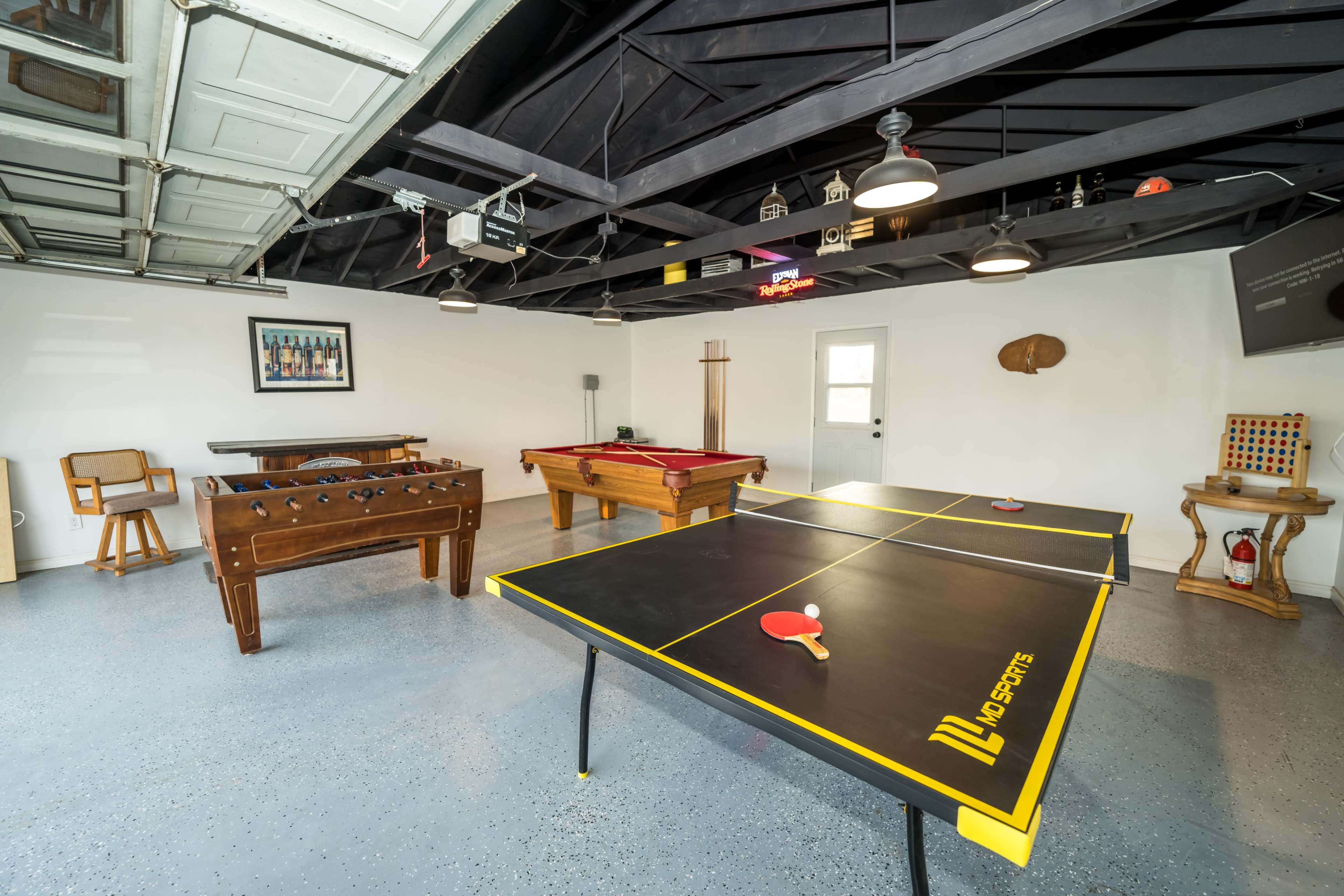 A spacious game room featuring a ping pong table, a foosball table, and a pool table, all set against a garage backdrop.