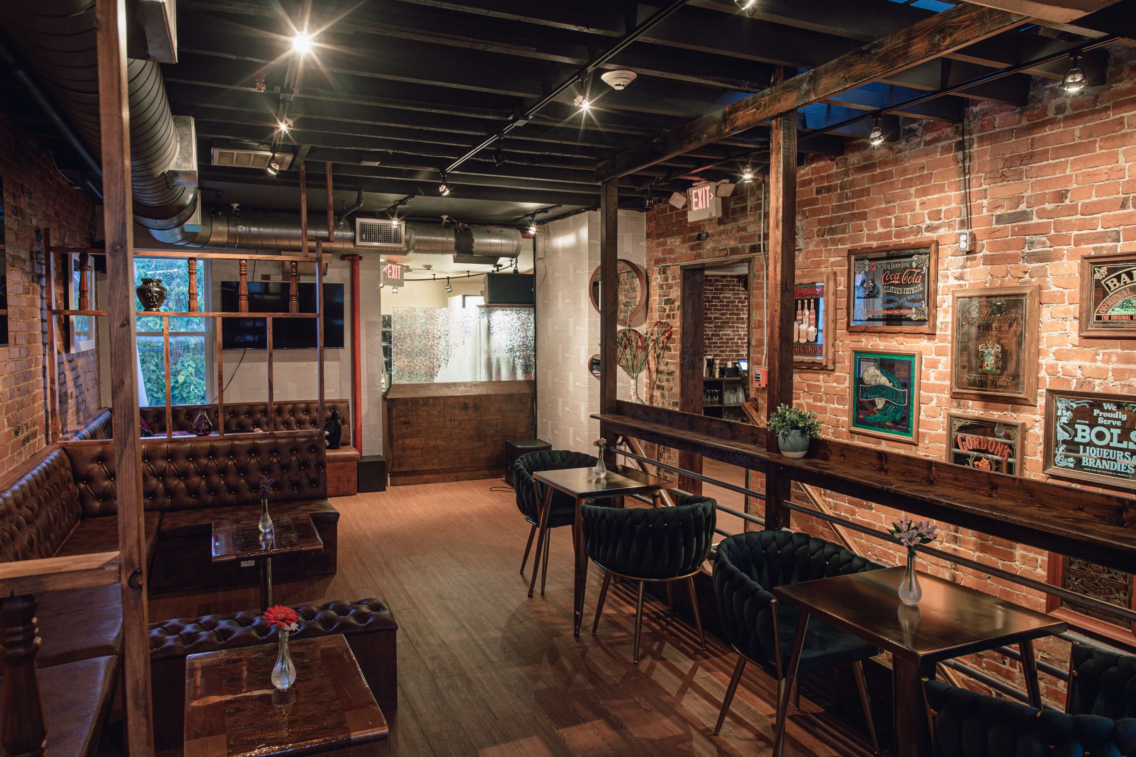 A rustic bar interior with exposed brick walls, wooden beams, and dark leather seating arranged around small tables.