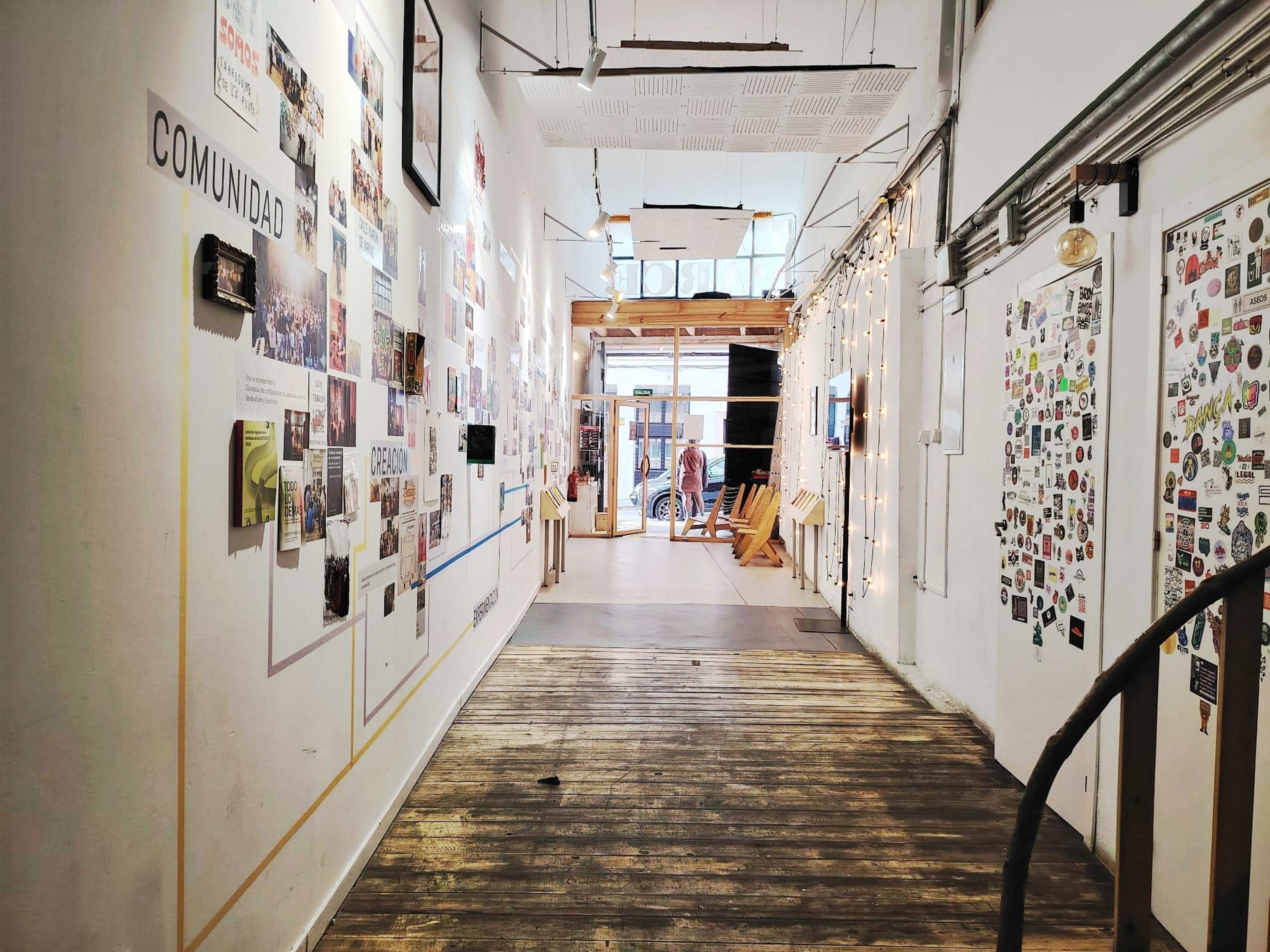 The image shows a hallway adorned with posters and photographs on the walls, leading towards an open area with wooden decor and visible people in the distance.