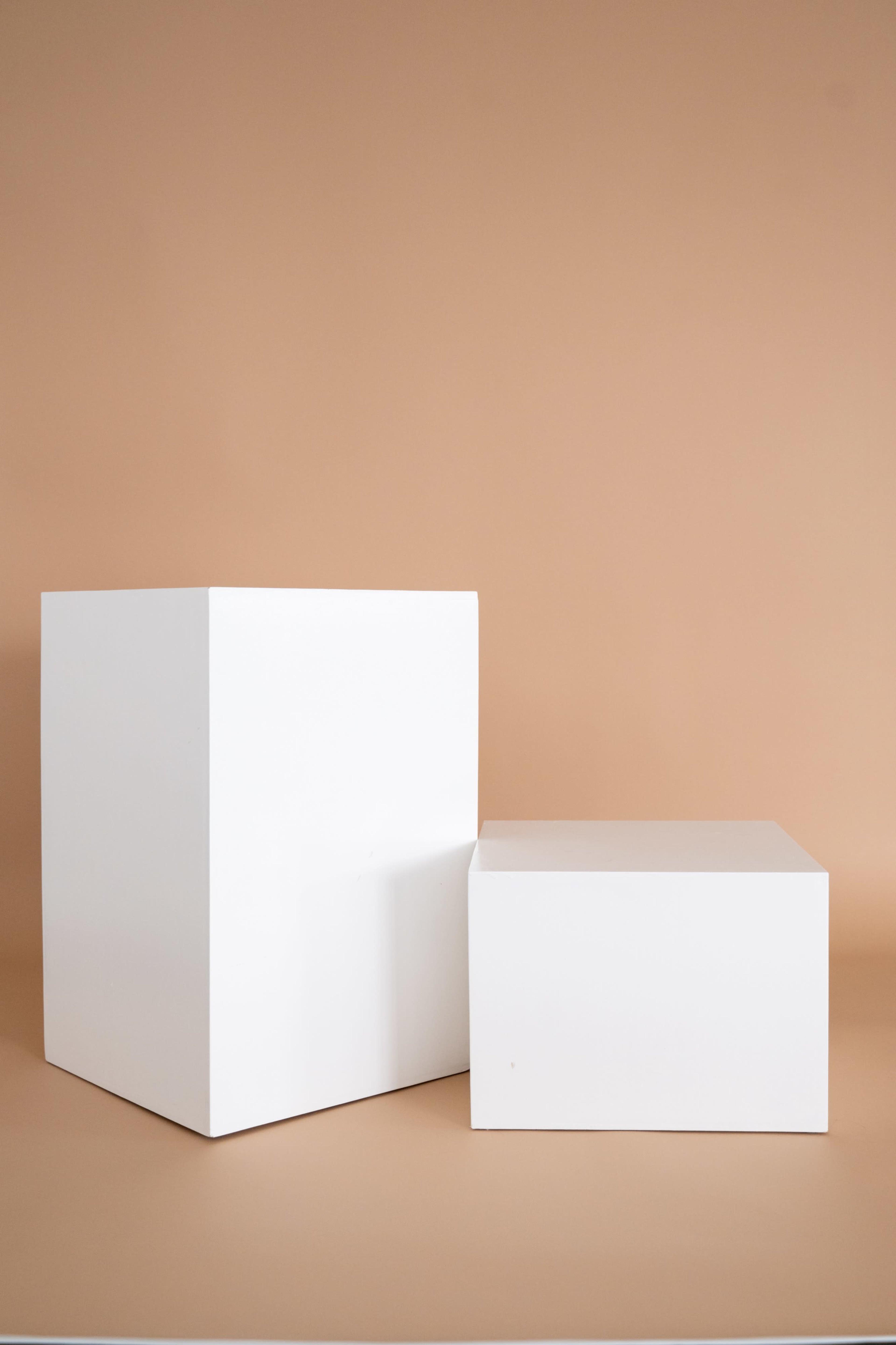 Two white geometric boxes of varying heights are positioned against a beige background.