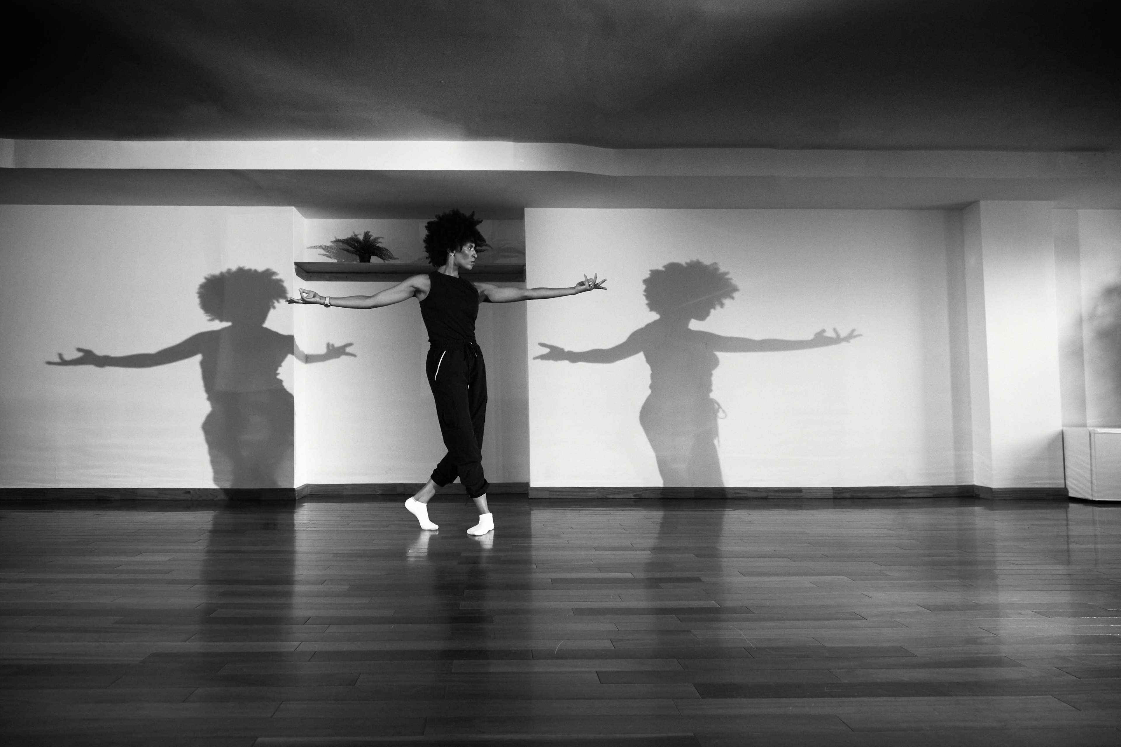 A dancer performs in an empty room, casting dynamic shadows on the wall behind them.