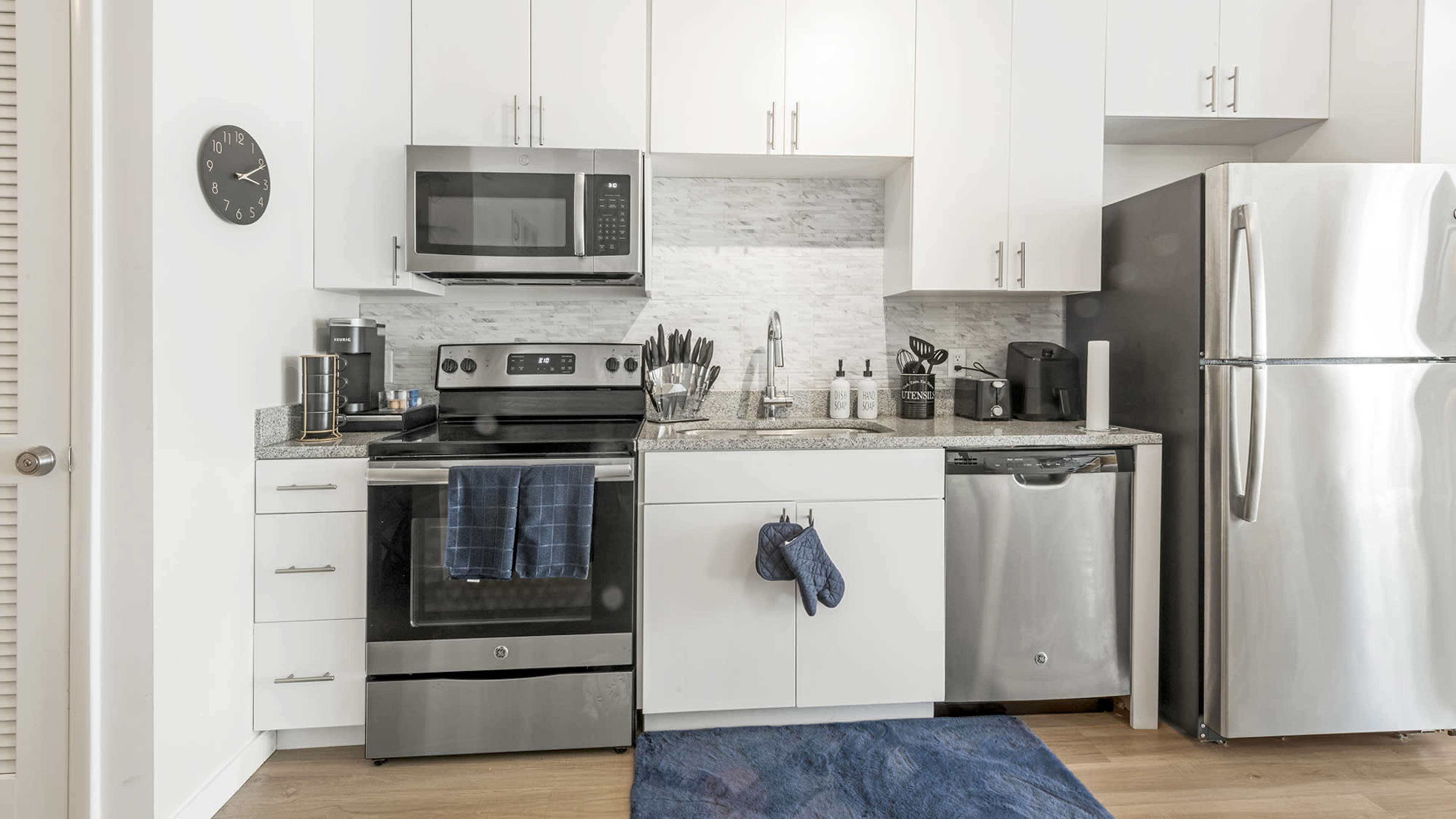 The image shows a modern kitchen featuring stainless steel appliances, white cabinetry, and a gray stone backsplash.