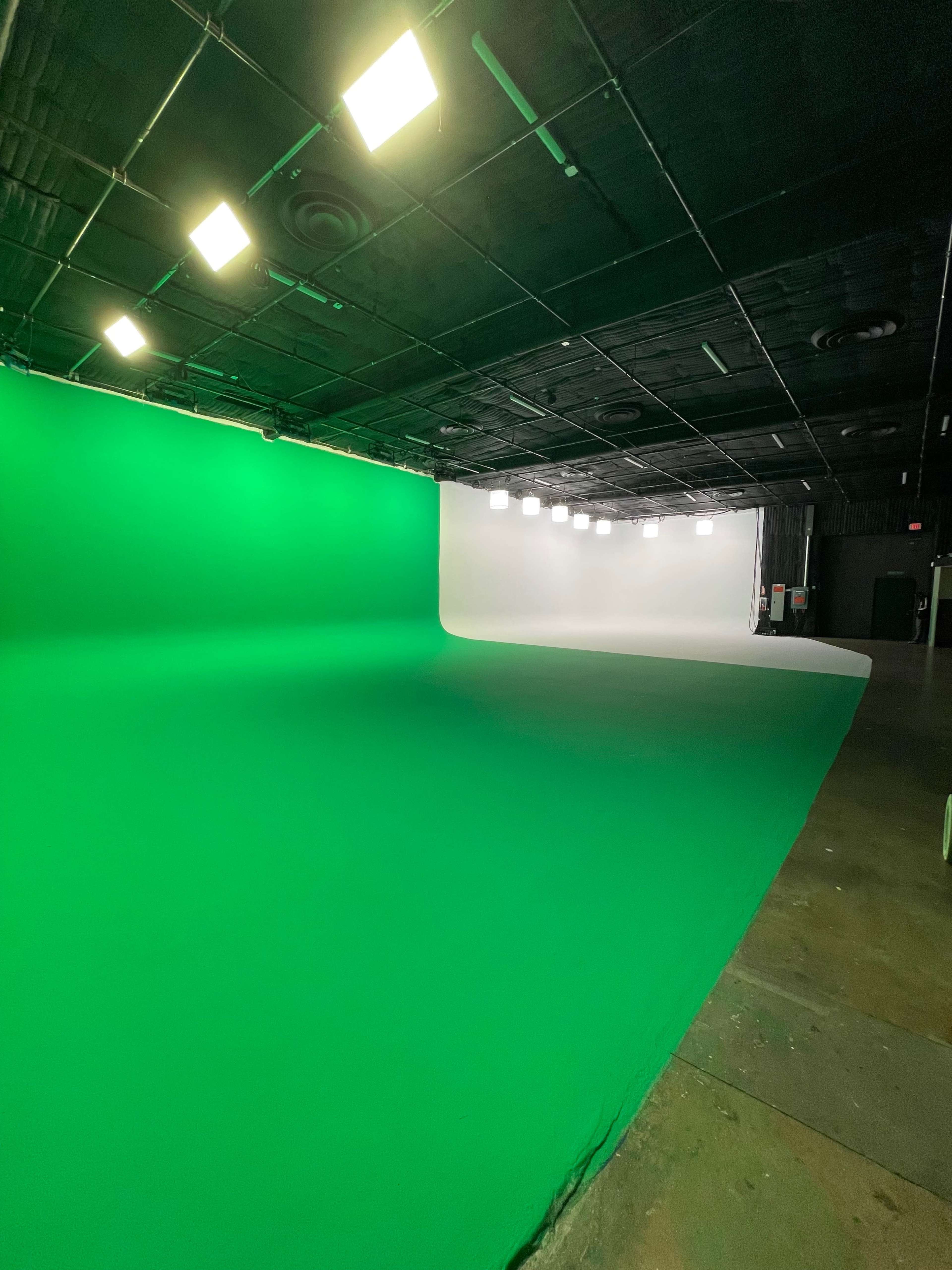 A studio space with a green backdrop on one side and a white backdrop on the other, illuminated by overhead lights.
