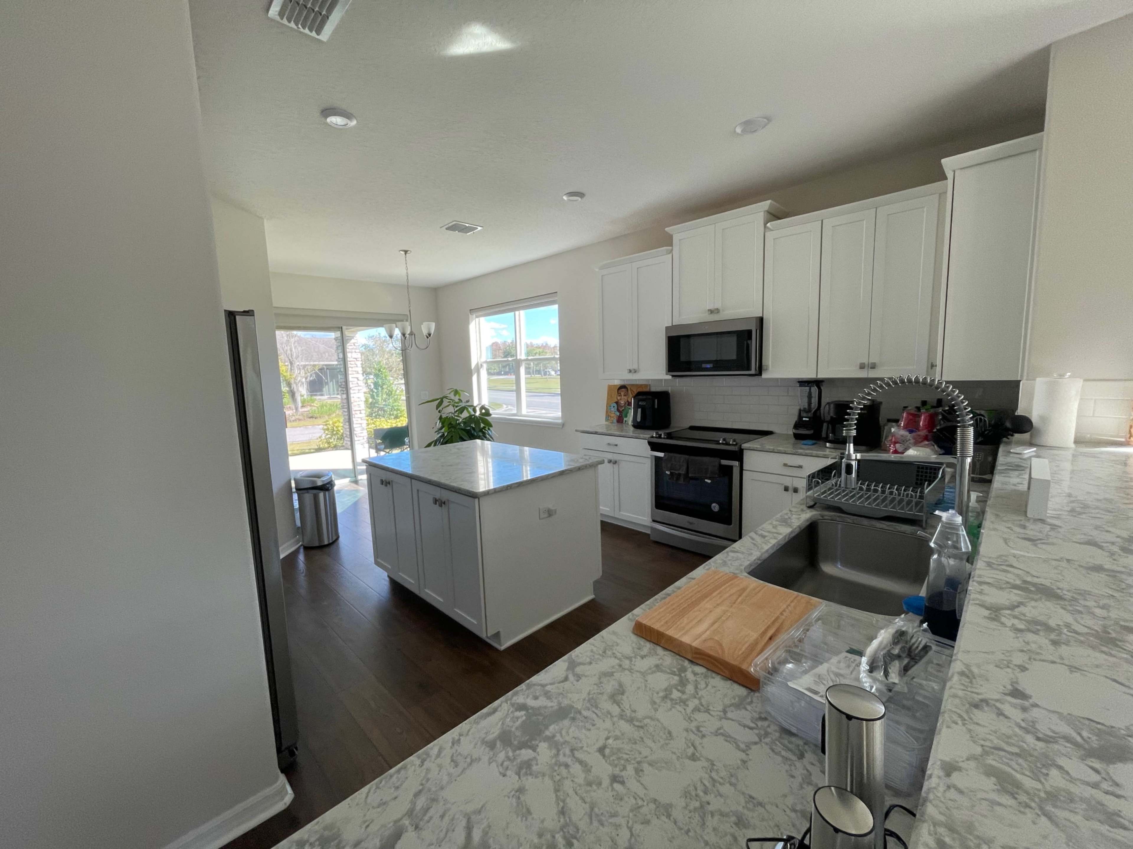 A modern kitchen with white cabinets, a marble countertop, and a central island, featuring a sink and appliances.