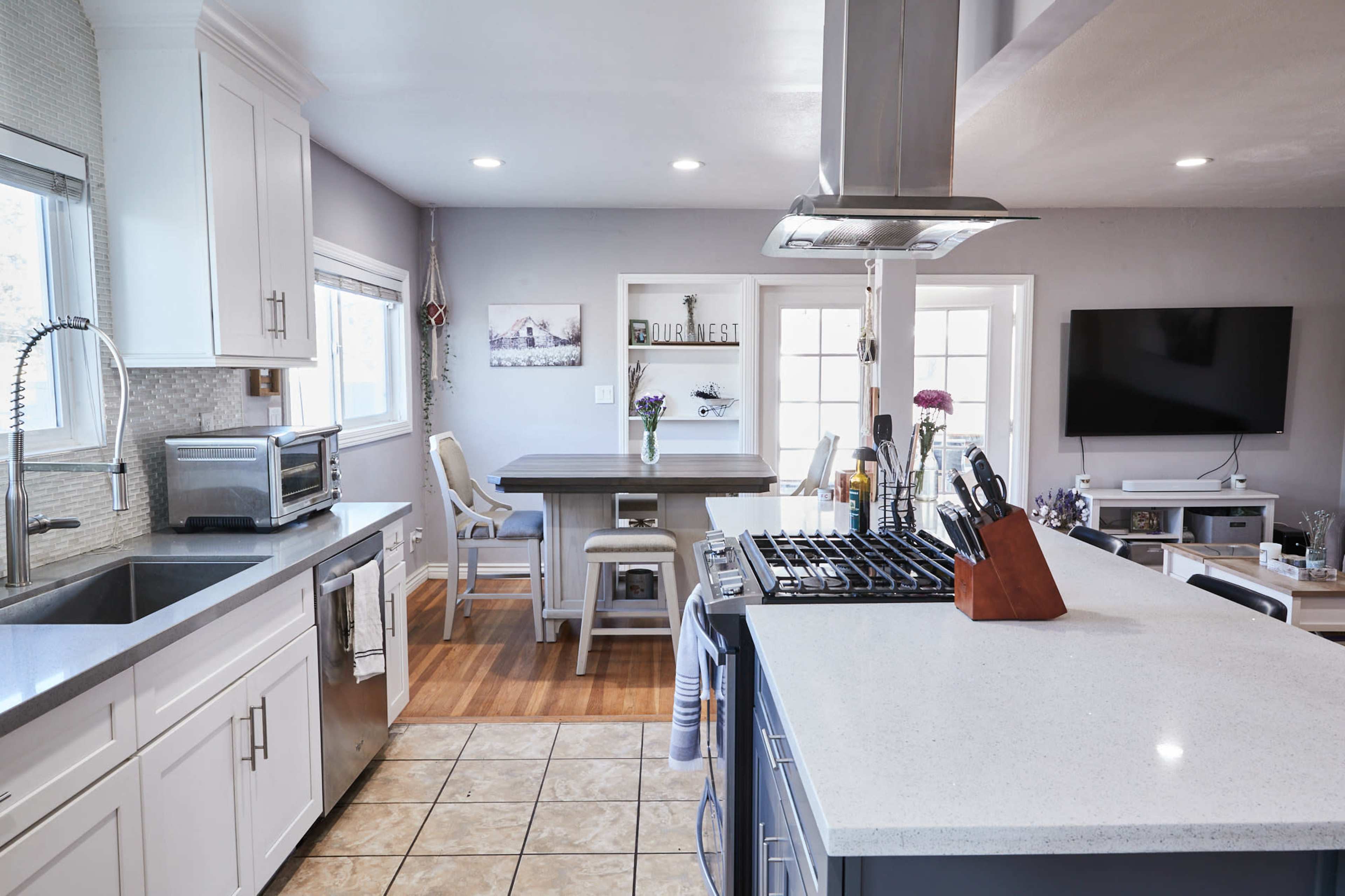 A modern kitchen features white cabinetry, stainless steel appliances, and a central island with a stove, adjacent to a dining area with a table and chairs.