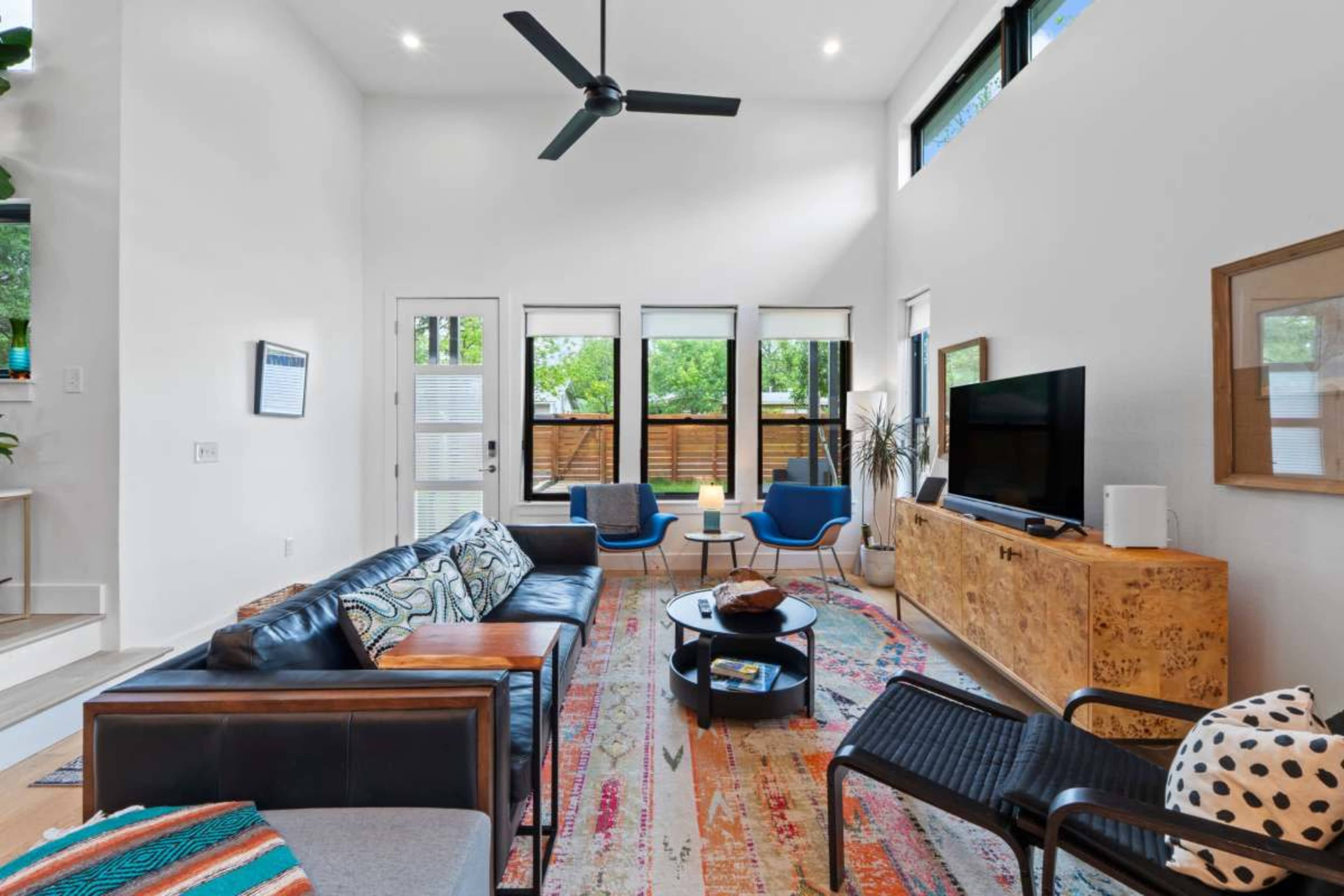 The living room features a modern design with a mix of seating options, large windows, and a central entertainment unit.