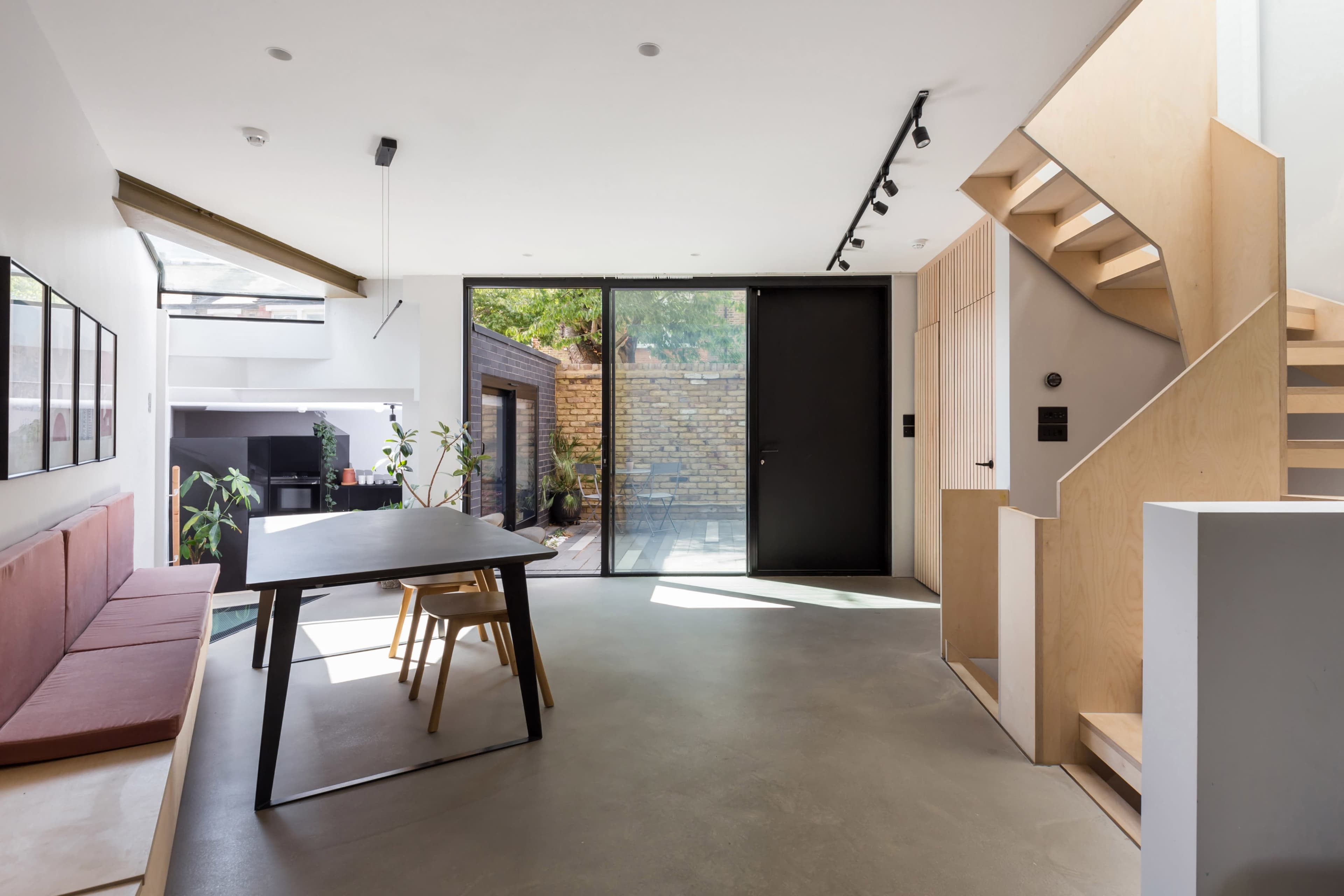 A modern interior space featuring a dining table with chairs, a staircase, a large glass door leading to a patio, and minimalistic decor.