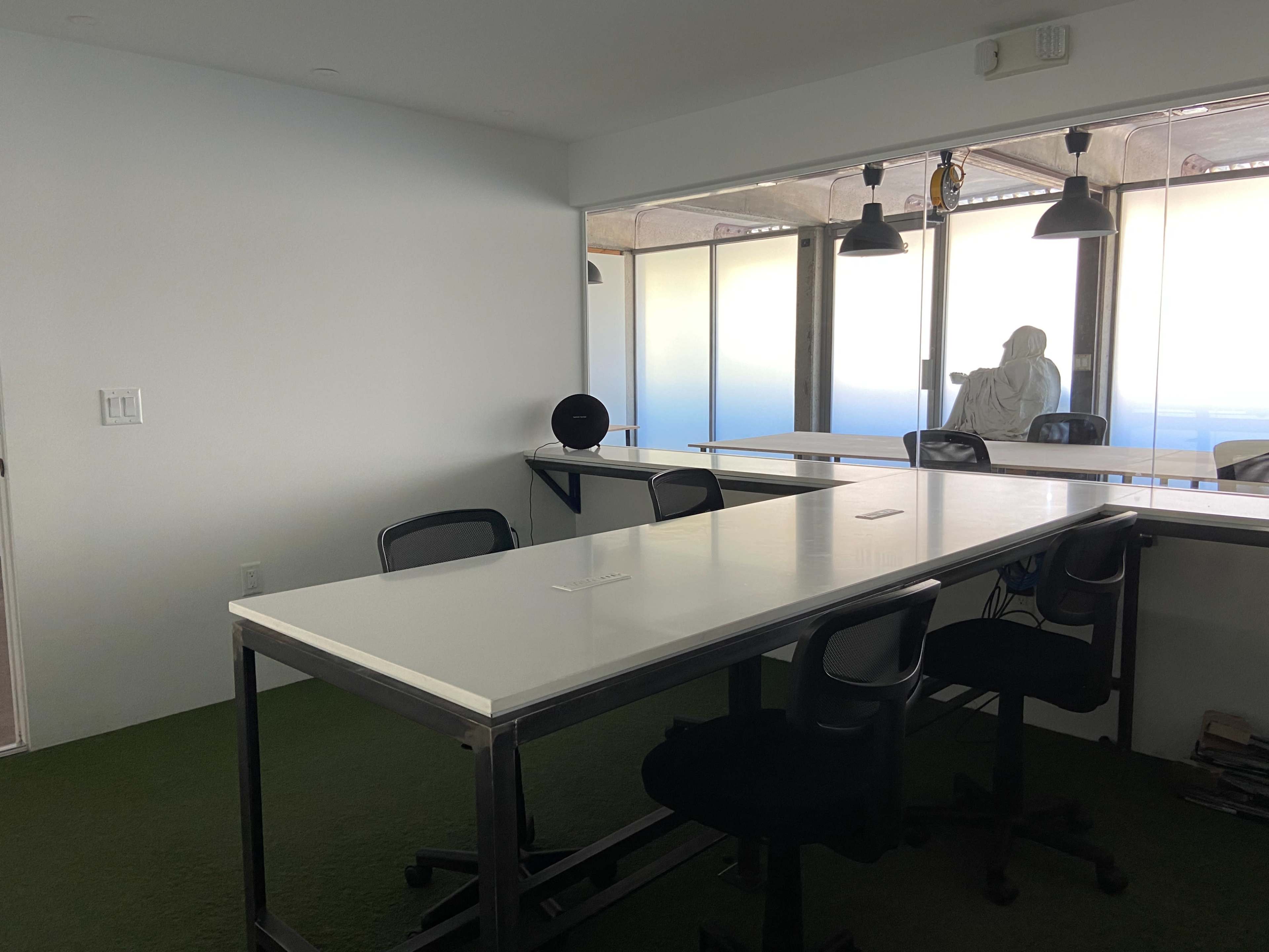 An empty, minimalist office space with a white table, black chairs, and large windows offering a view.