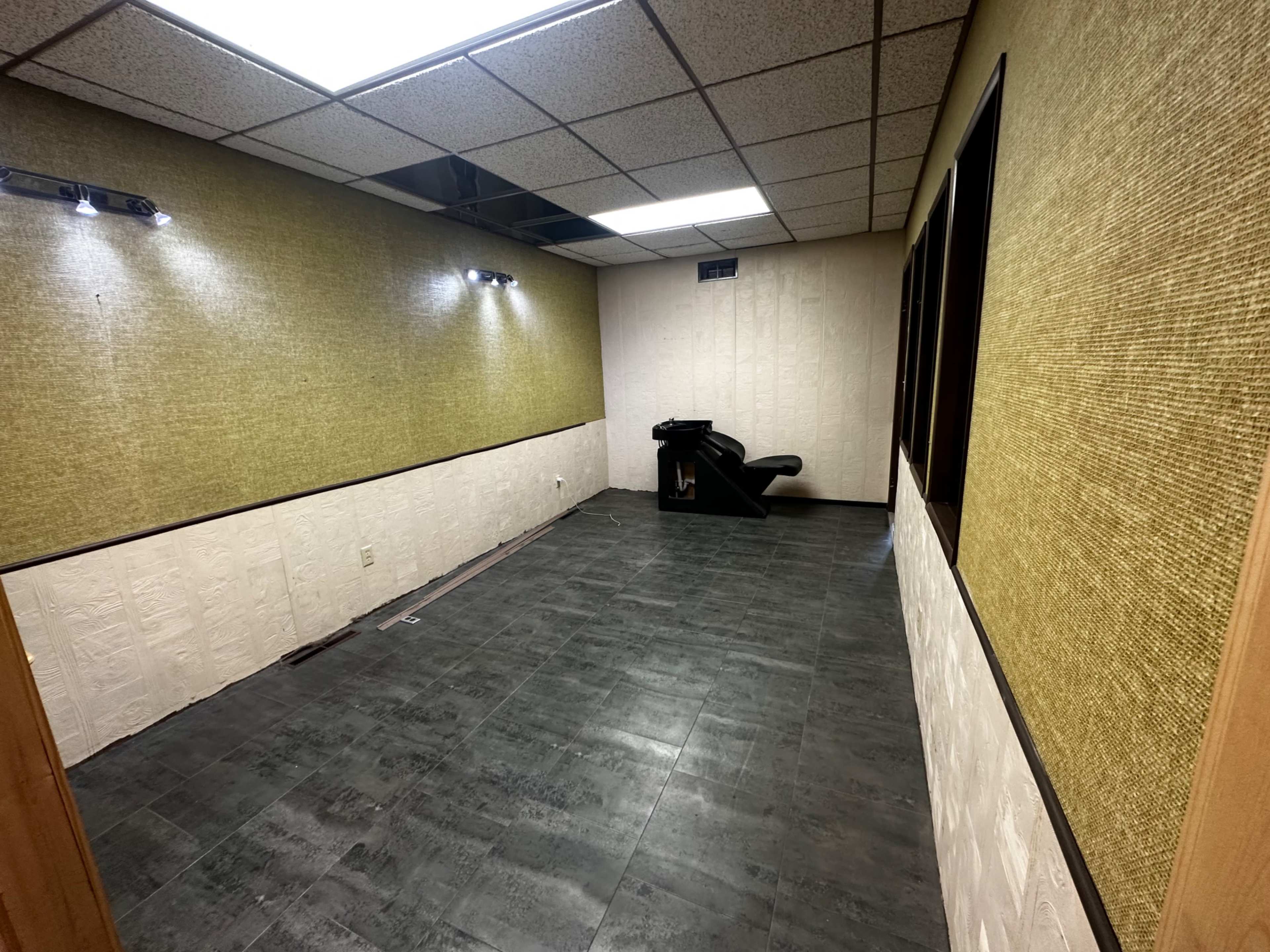 The image shows an empty room with a tiled floor, textured walls, and minimal lighting.