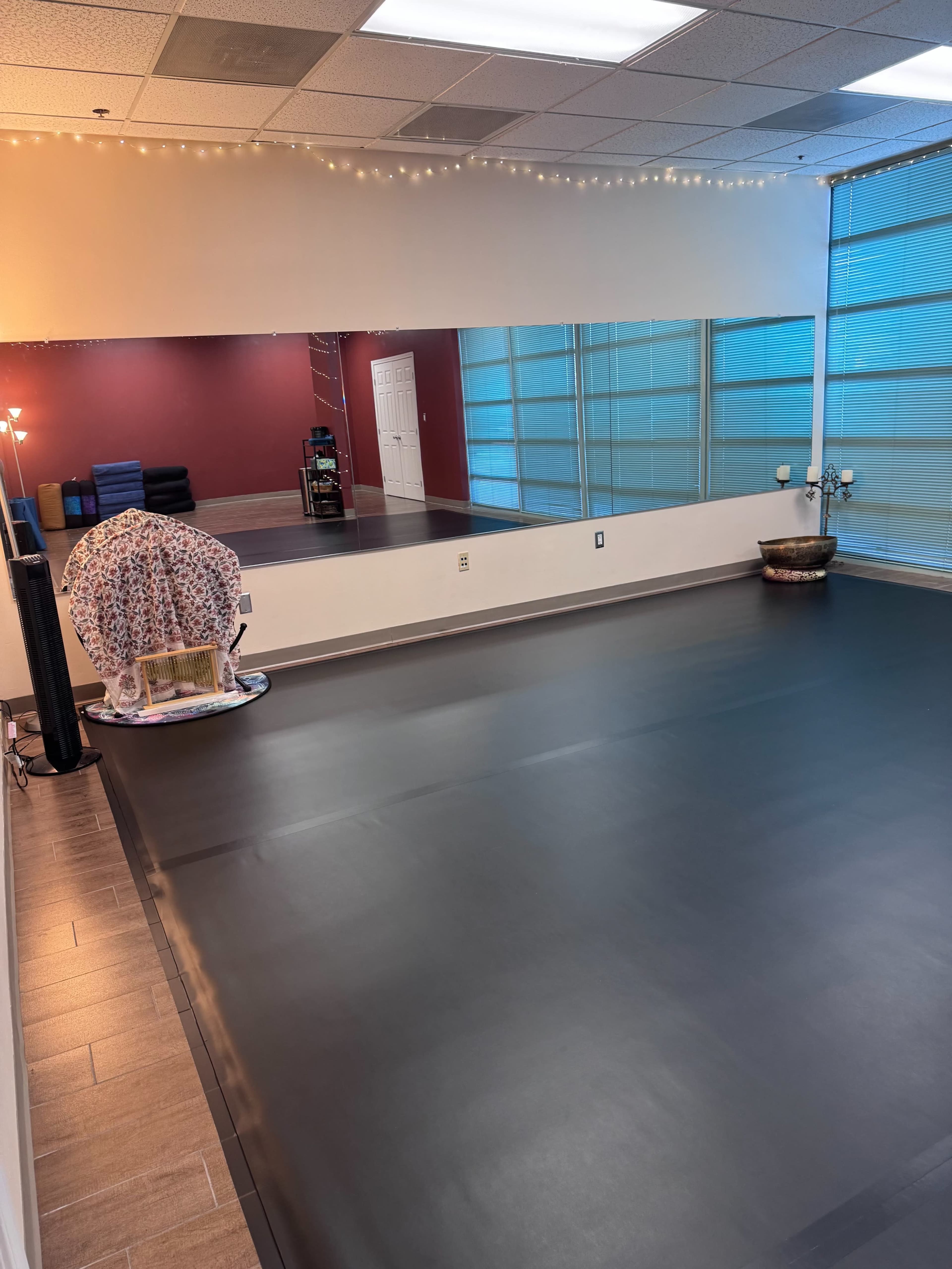 The image shows an empty studio space with a black floor, a large mirror on one wall, and natural light coming through windows.