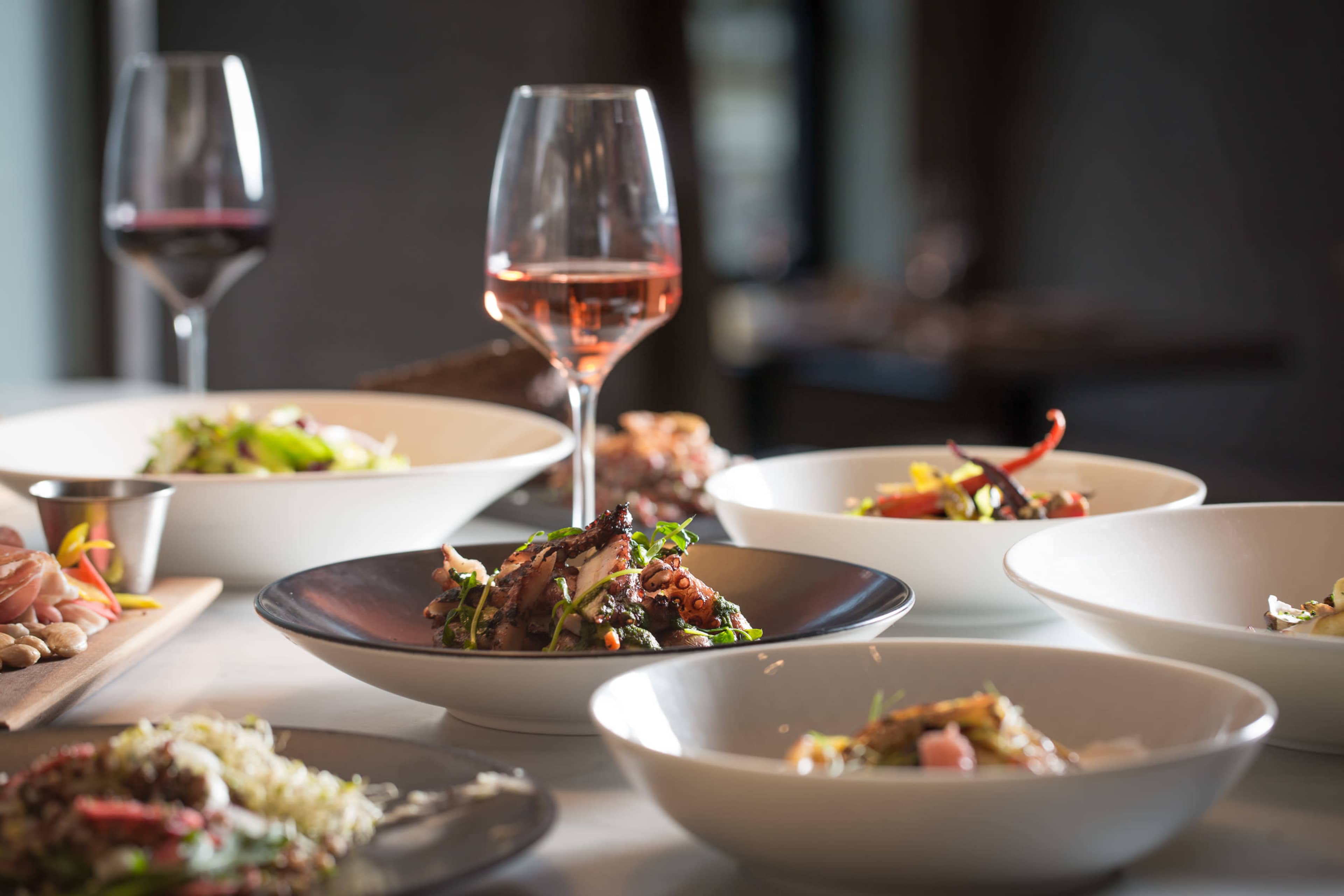 The image features a variety of elegantly arranged dishes alongside a glass of rosé wine, set on a table.