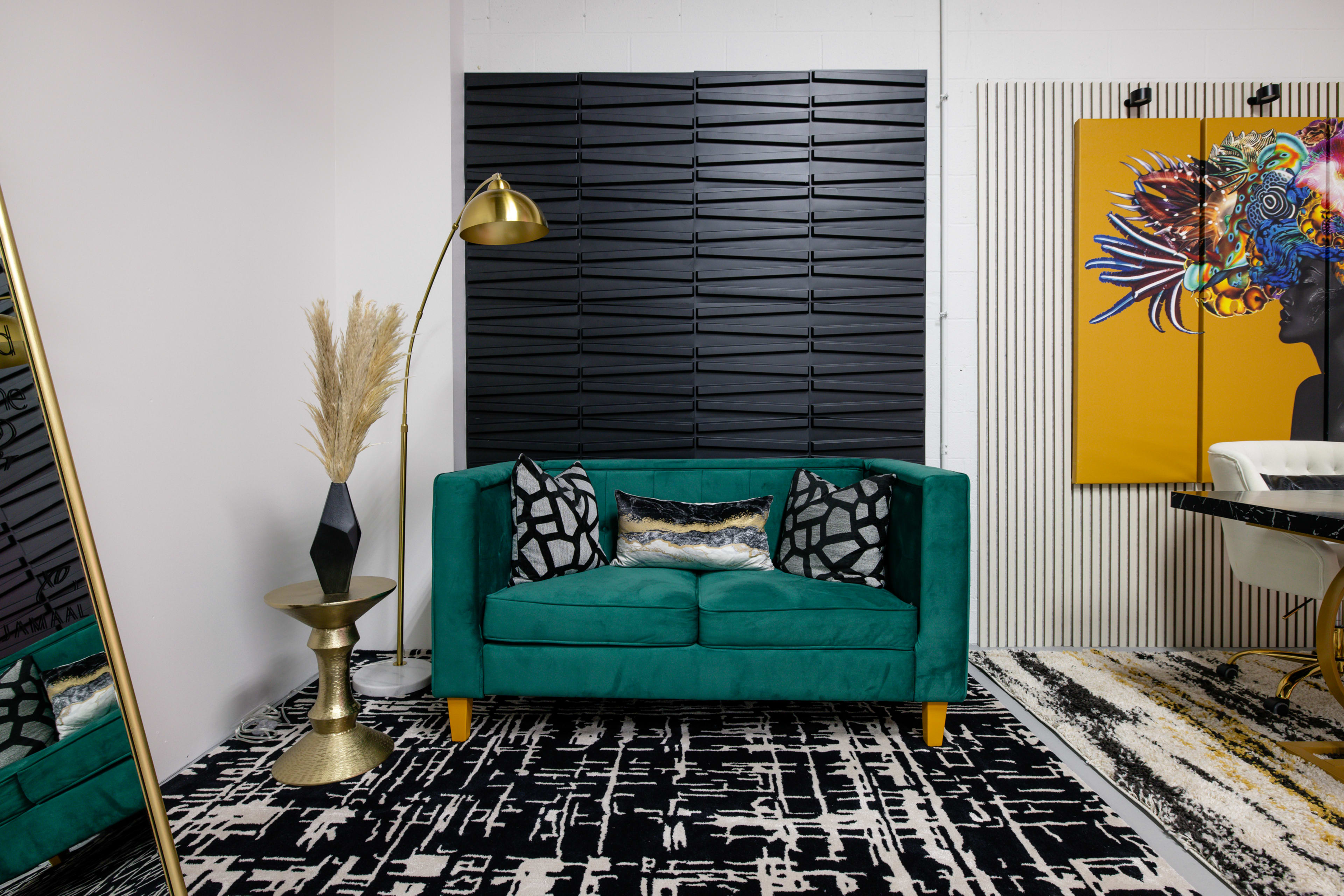 A green sofa with decorative pillows, a gold floor lamp, a patterned area rug, and a wall with black decorative panels.