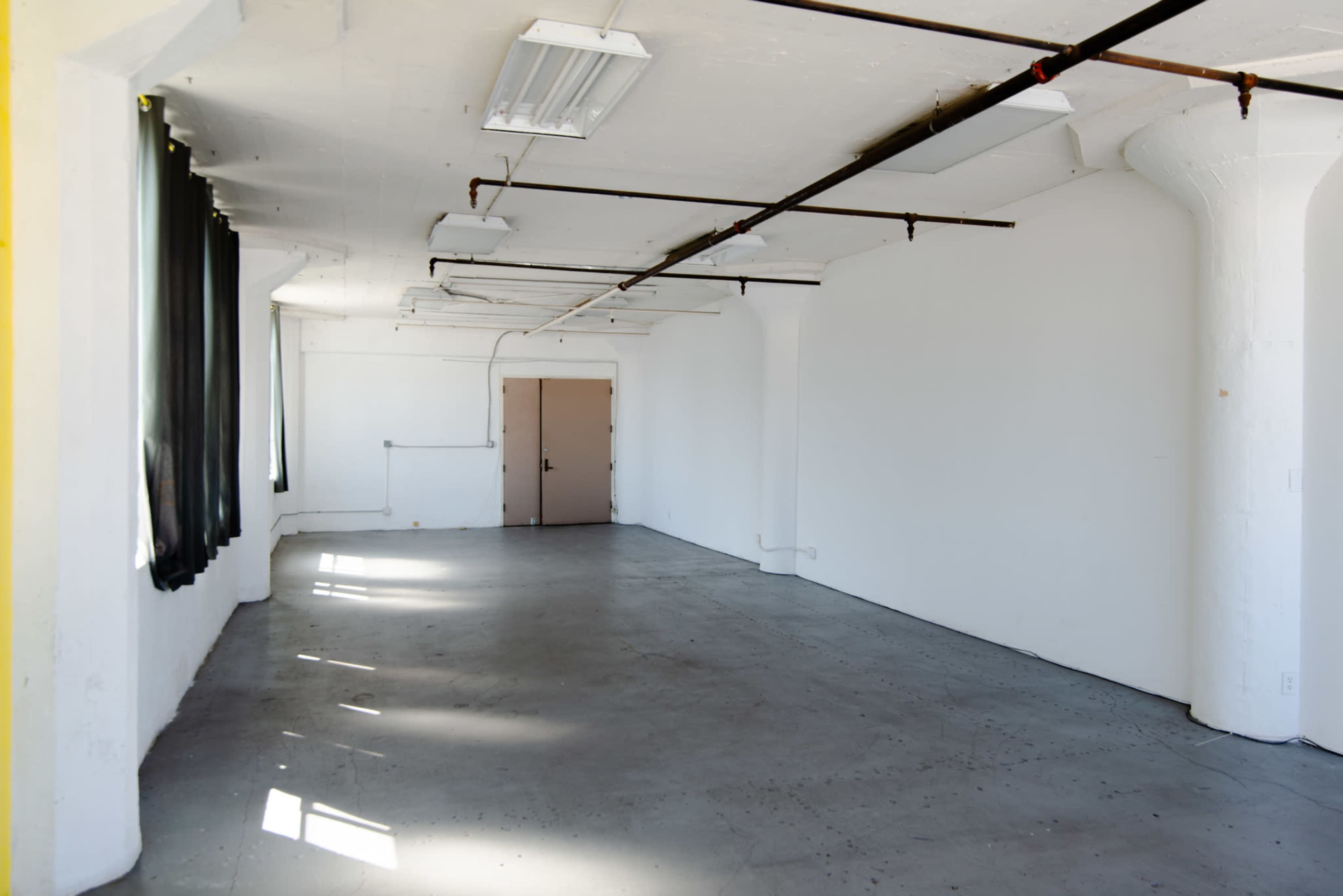 An empty room with white walls, concrete flooring, and scattered beams of sunlight coming through windows.
