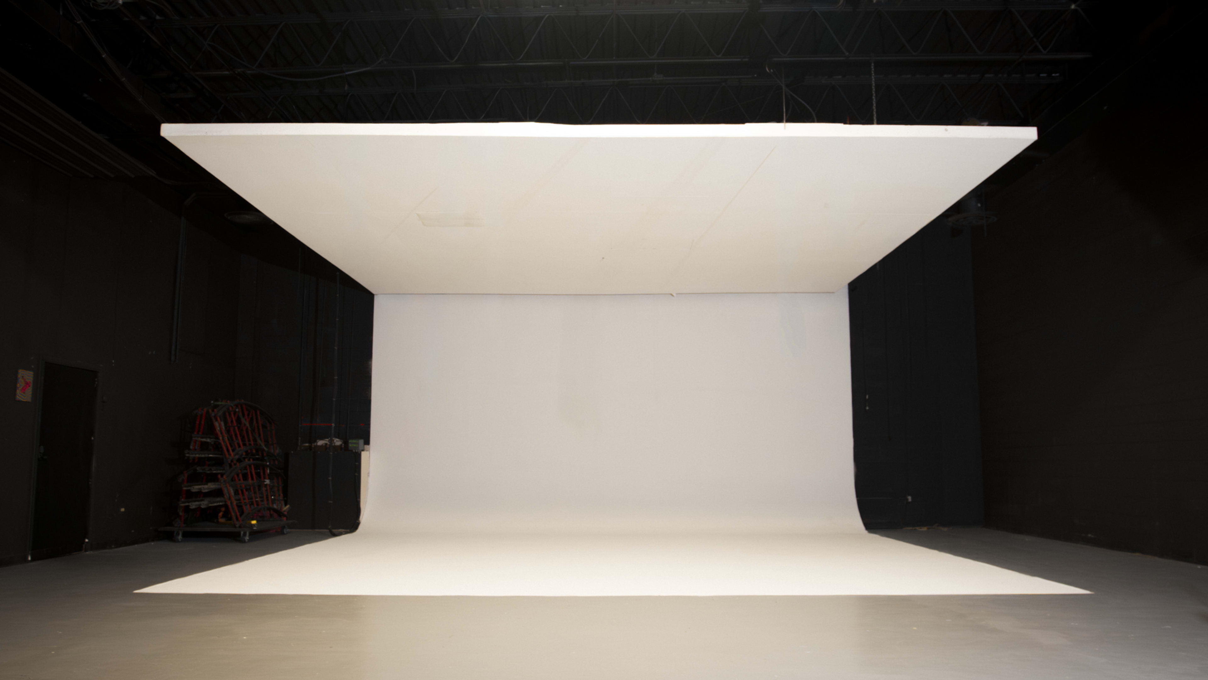 The image shows an empty photography studio with a large, flat backdrop and a seamless white floor.