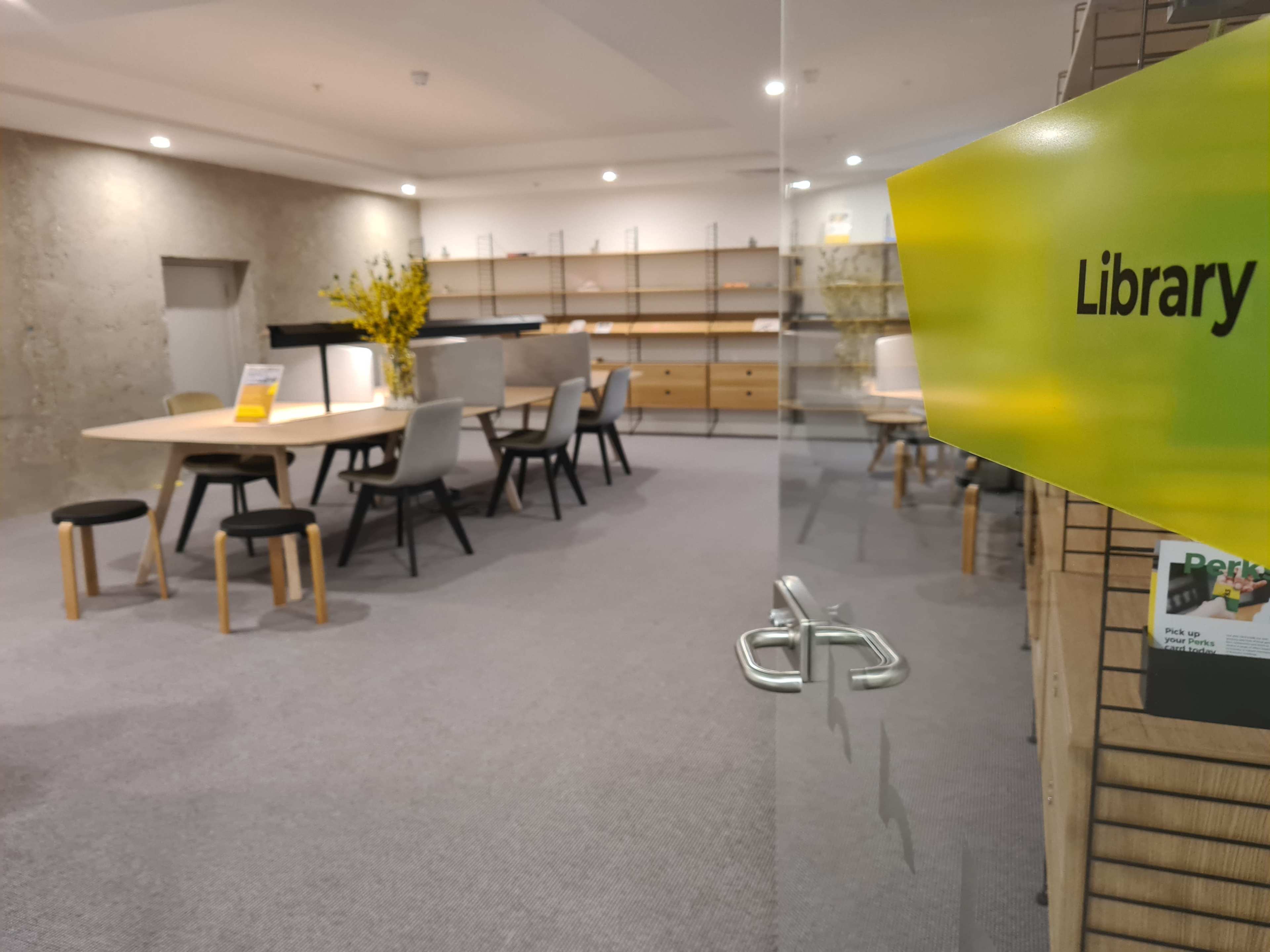 A modern library space featuring a large wooden table, several chairs, and shelves displaying books and decorative items.