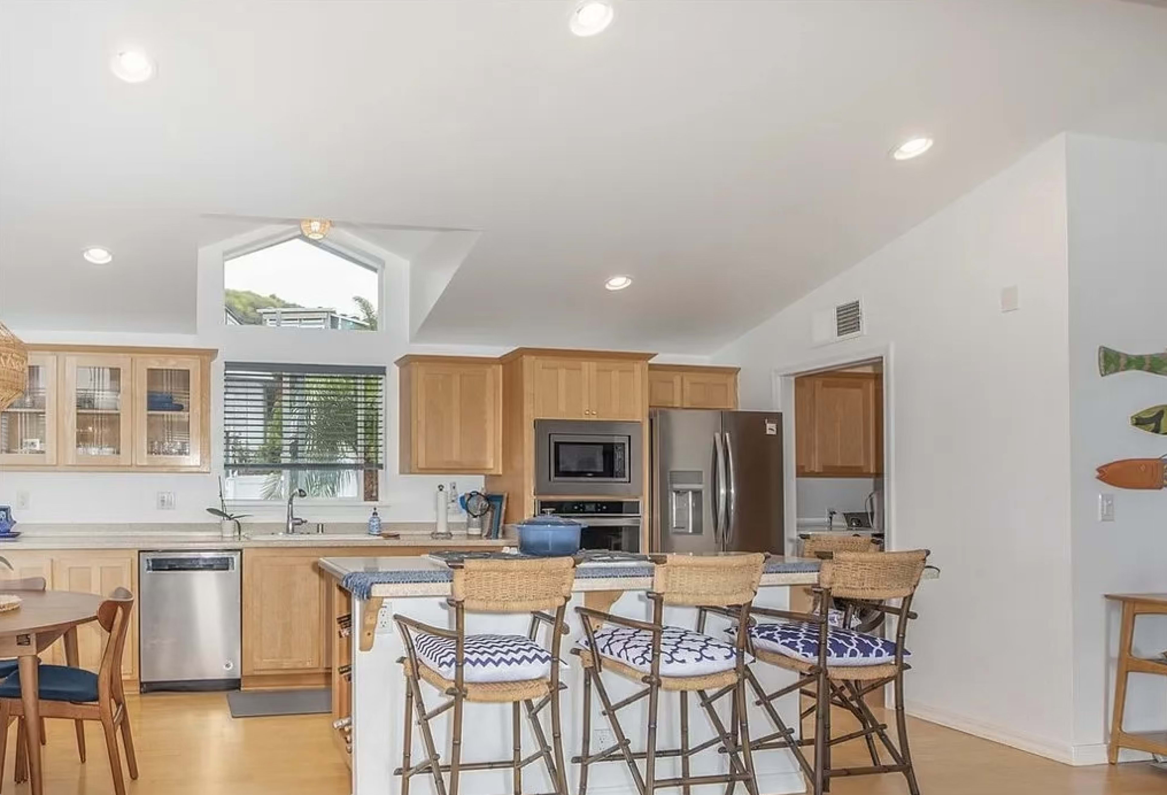 A modern kitchen with wooden cabinetry, a central island with barstools, and stainless steel appliances.