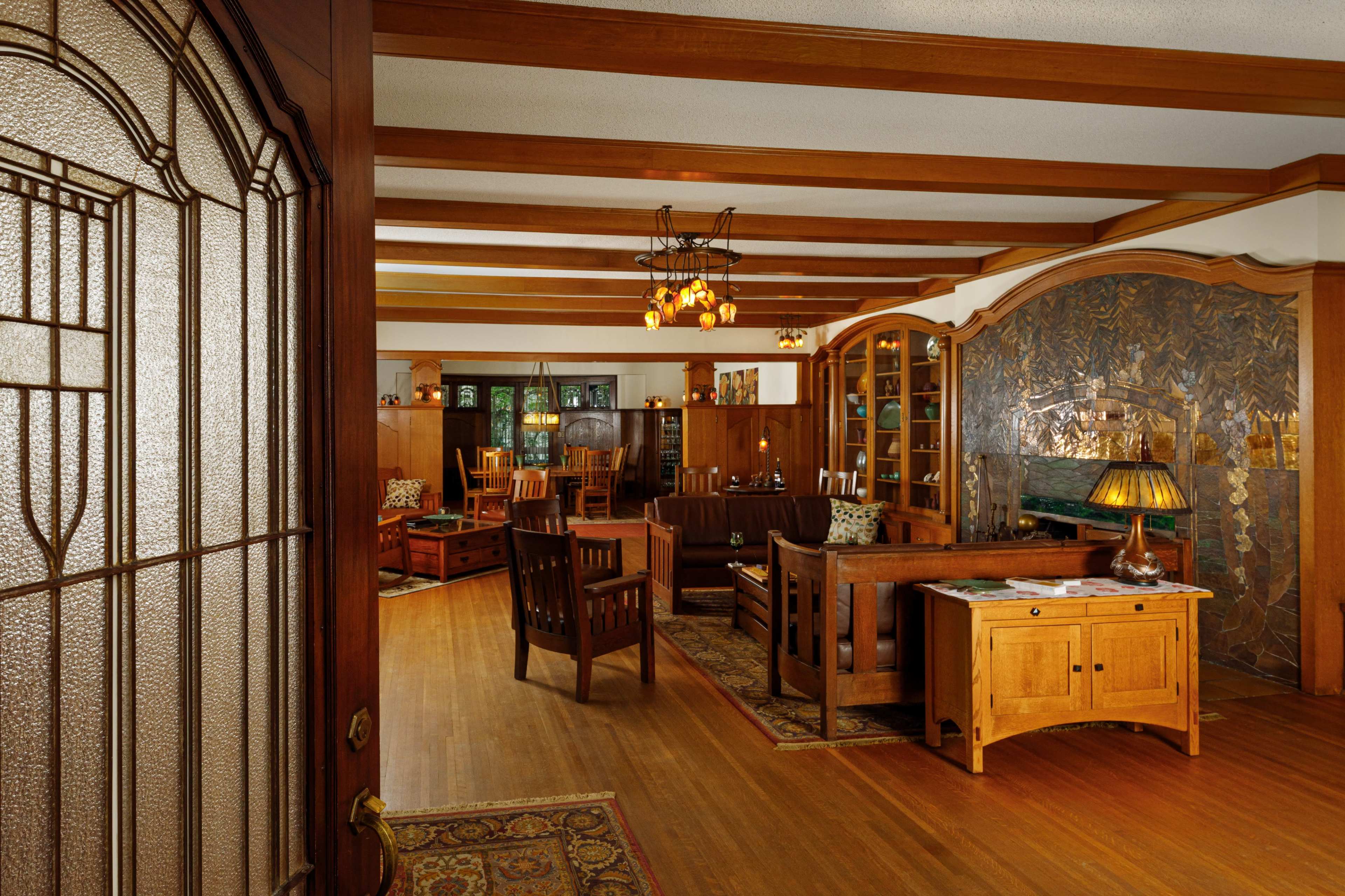 A warmly lit interior of a traditional living room featuring wooden furniture, a patterned rug, and decorative wall art.