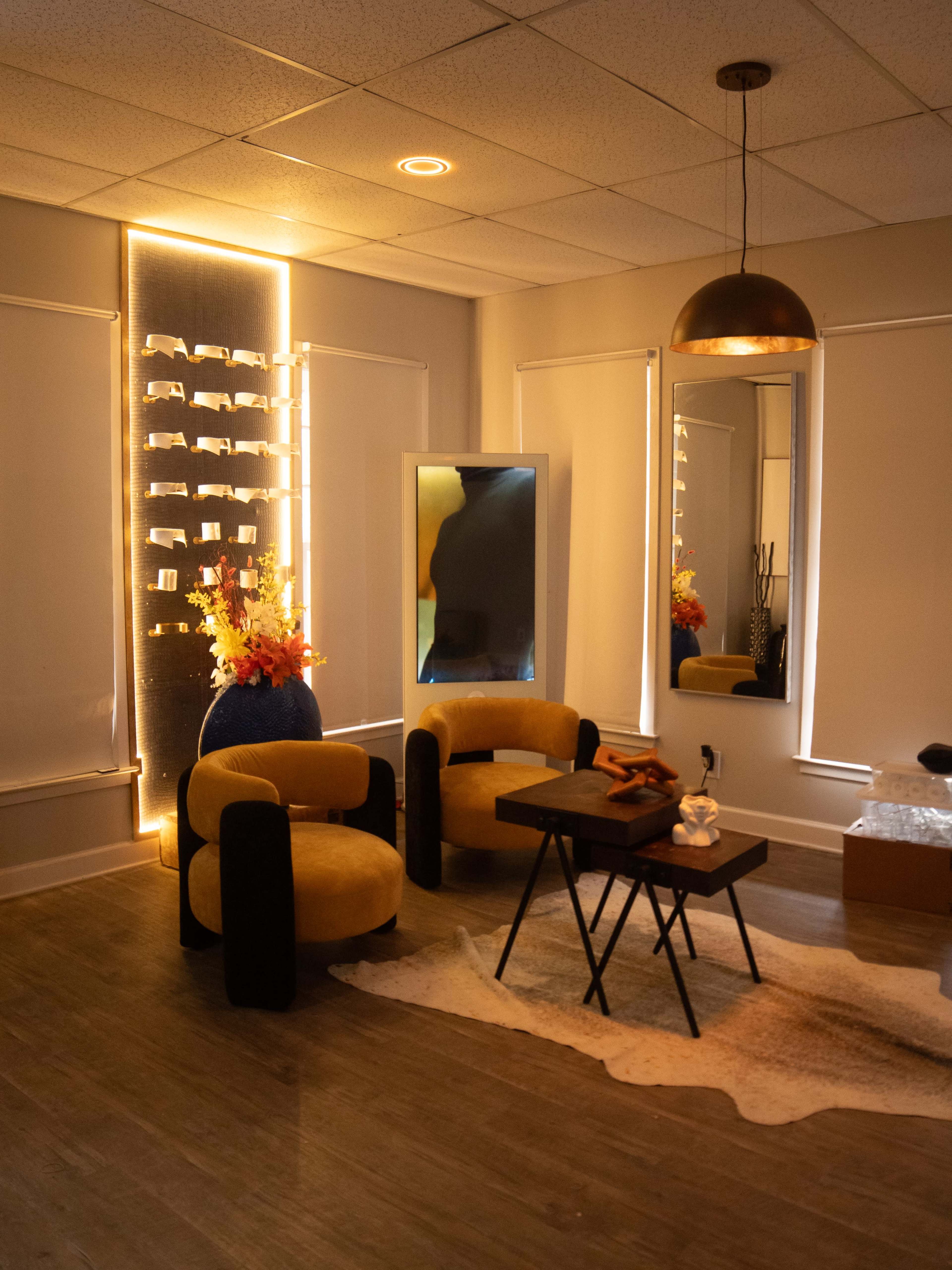 The image shows a modern, well-lit room featuring two yellow chairs, a small black table, and decorative elements with a plant and artificial flowers.