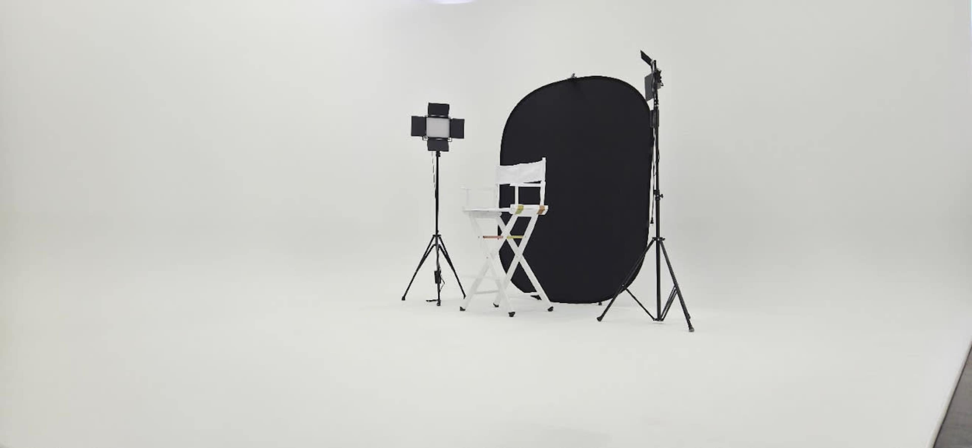 The image shows a photography studio with a white backdrop, a black backdrop, a director's chair, and lighting equipment.
