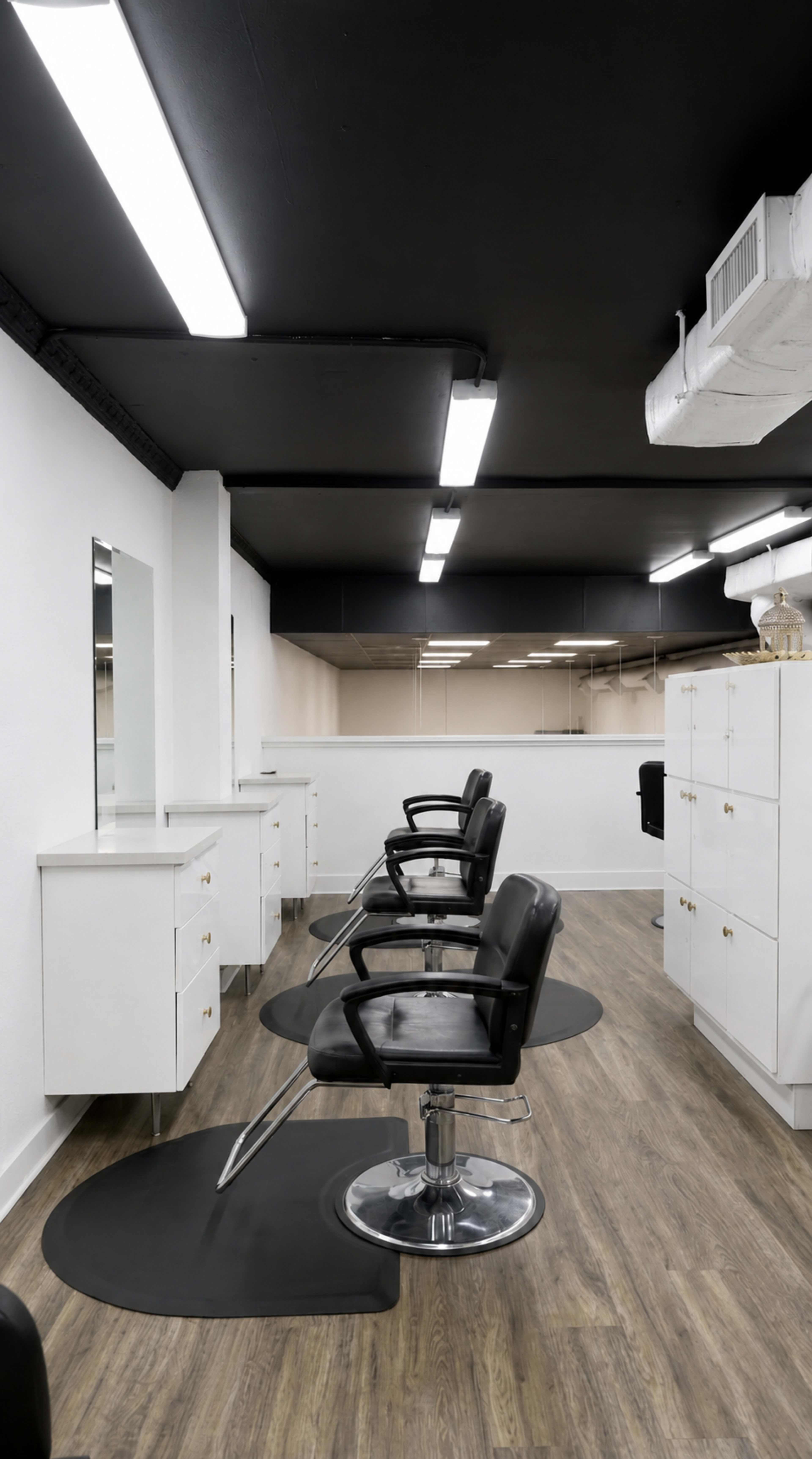 The image shows a modern hair salon with black chairs, styling stations, and bright overhead lighting.