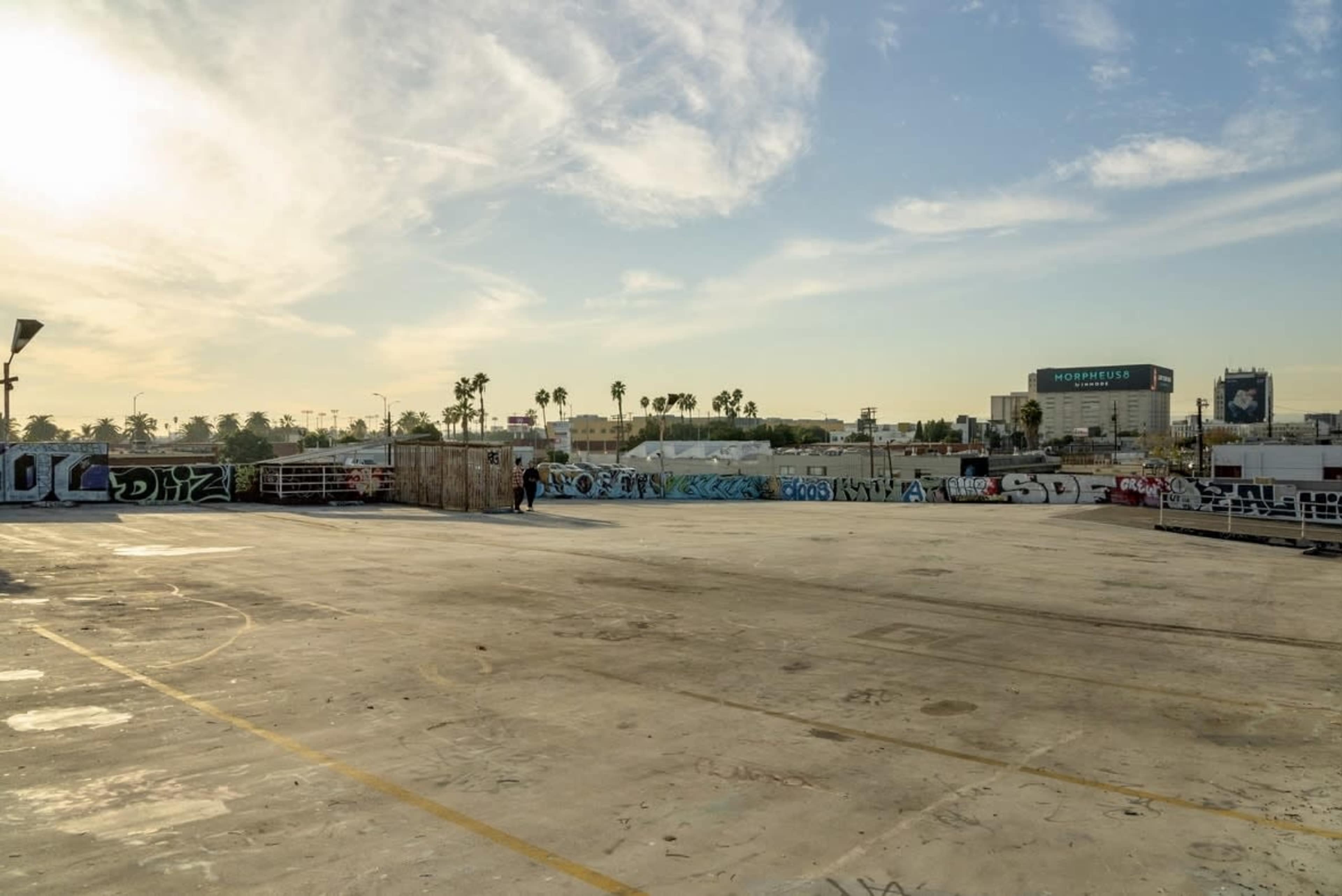 The image shows a wide, empty rooftop space with graffiti-covered walls and palm trees in the background under a clear sky.