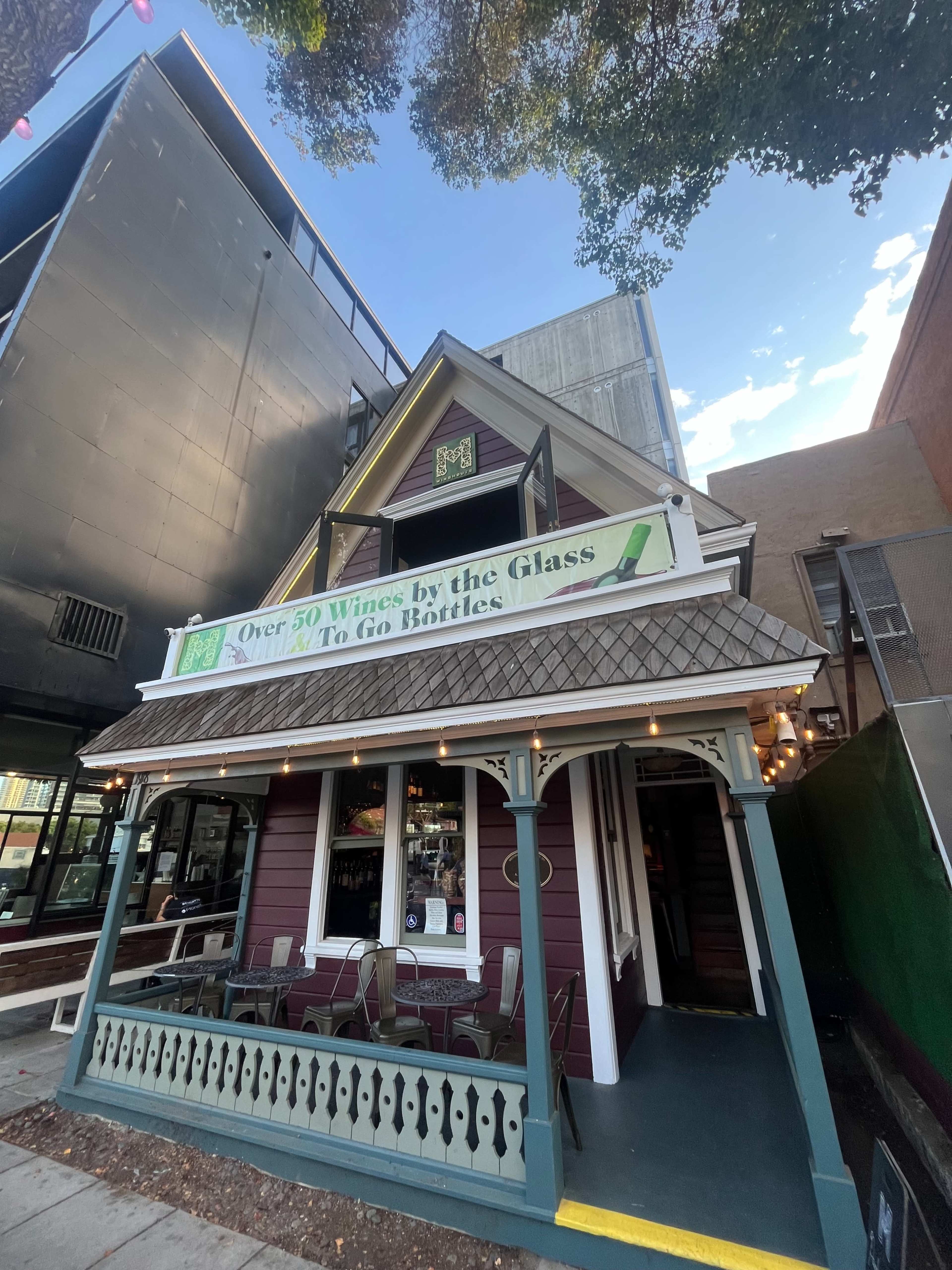 A quaint, two-story building with a porch displays a sign advertising over 50 wines by the glass and bottles to go.