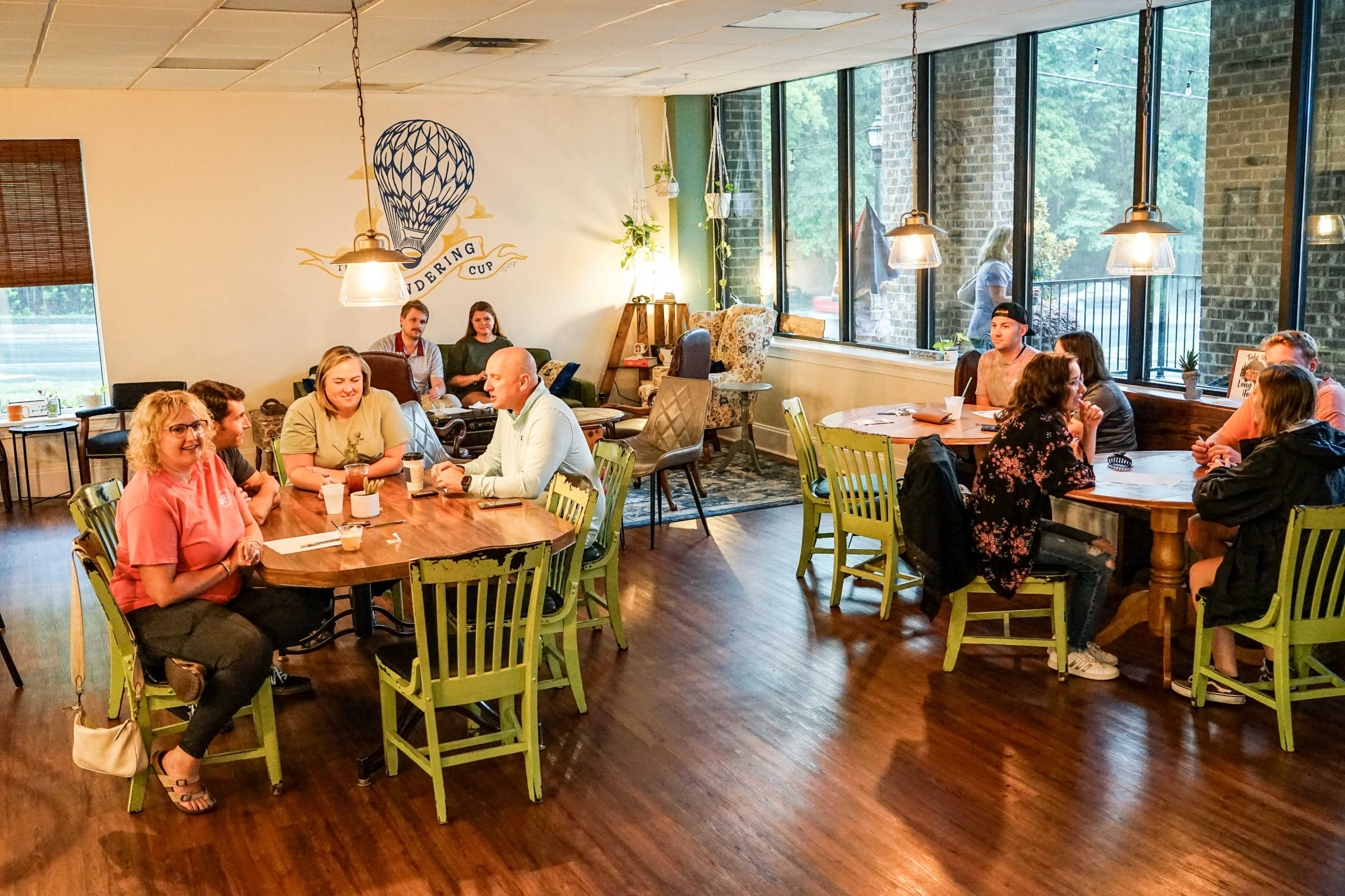A cozy café interior with groups of people sitting at wooden tables, enjoying drinks and conversations under warm lighting.