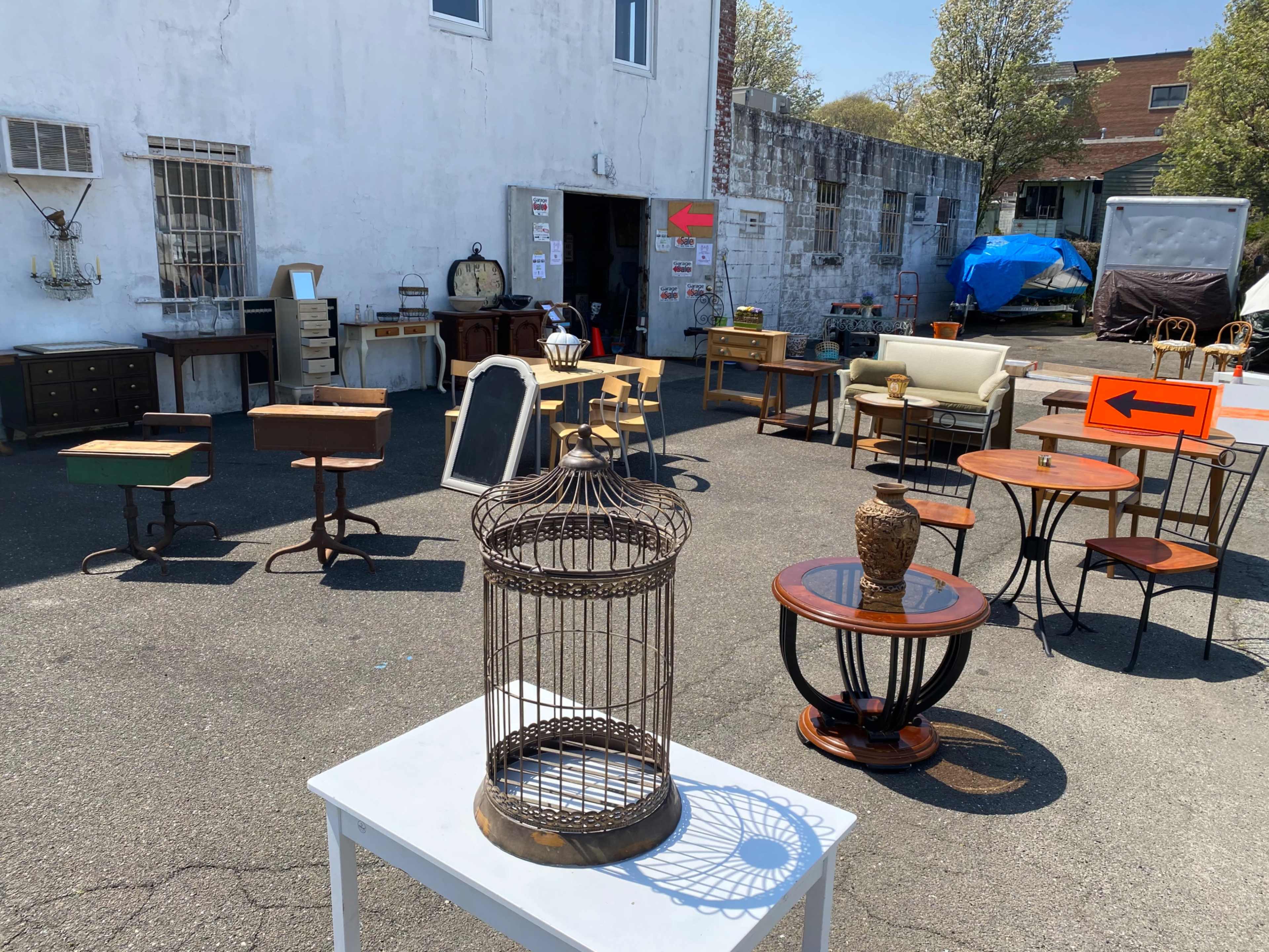 An outdoor furniture sale with various pieces, including tables, chairs, and a birdcage, displayed in a parking area.