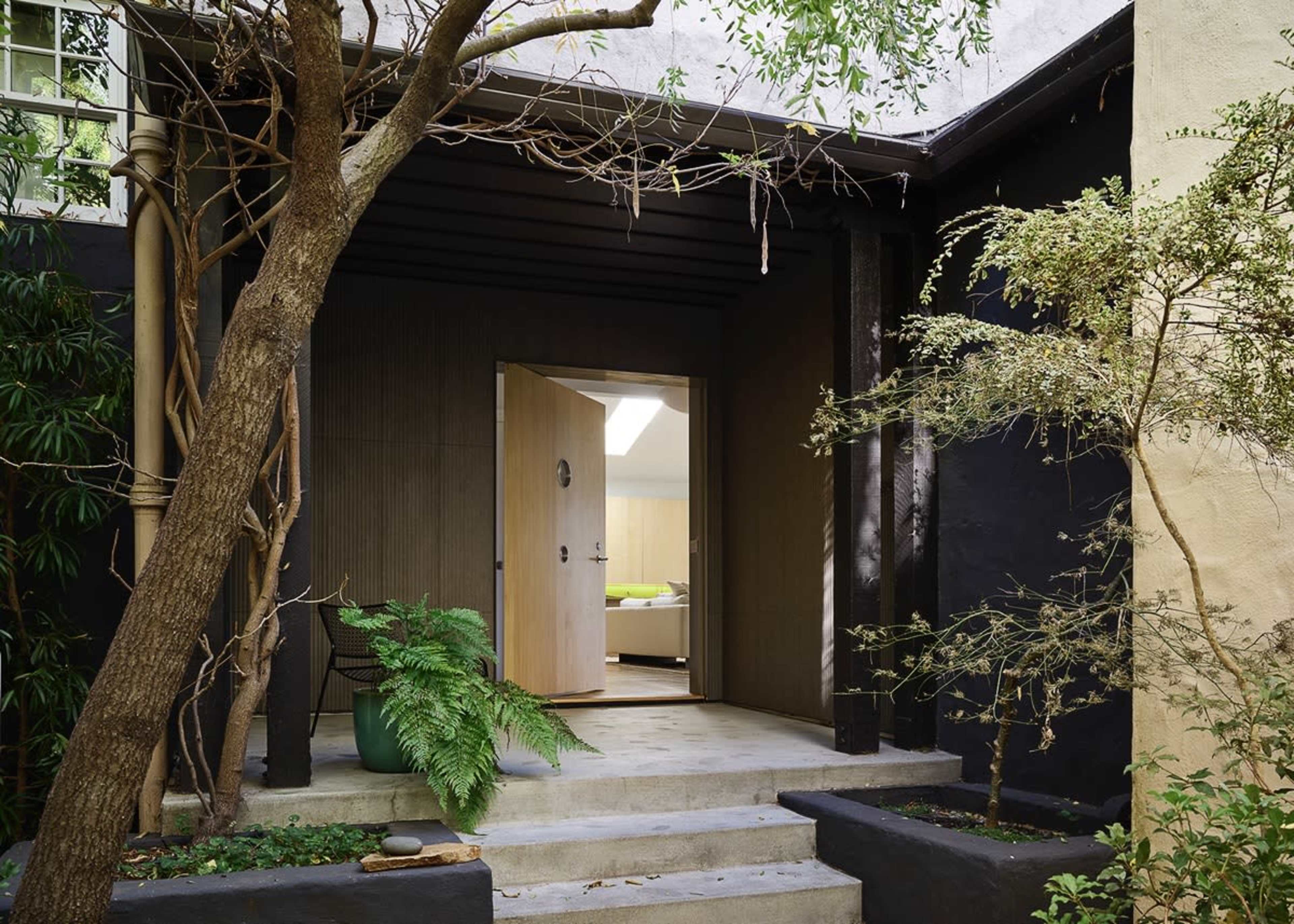 The image shows the entrance of a modern home framed by greenery and accentuated by a large door at the center.