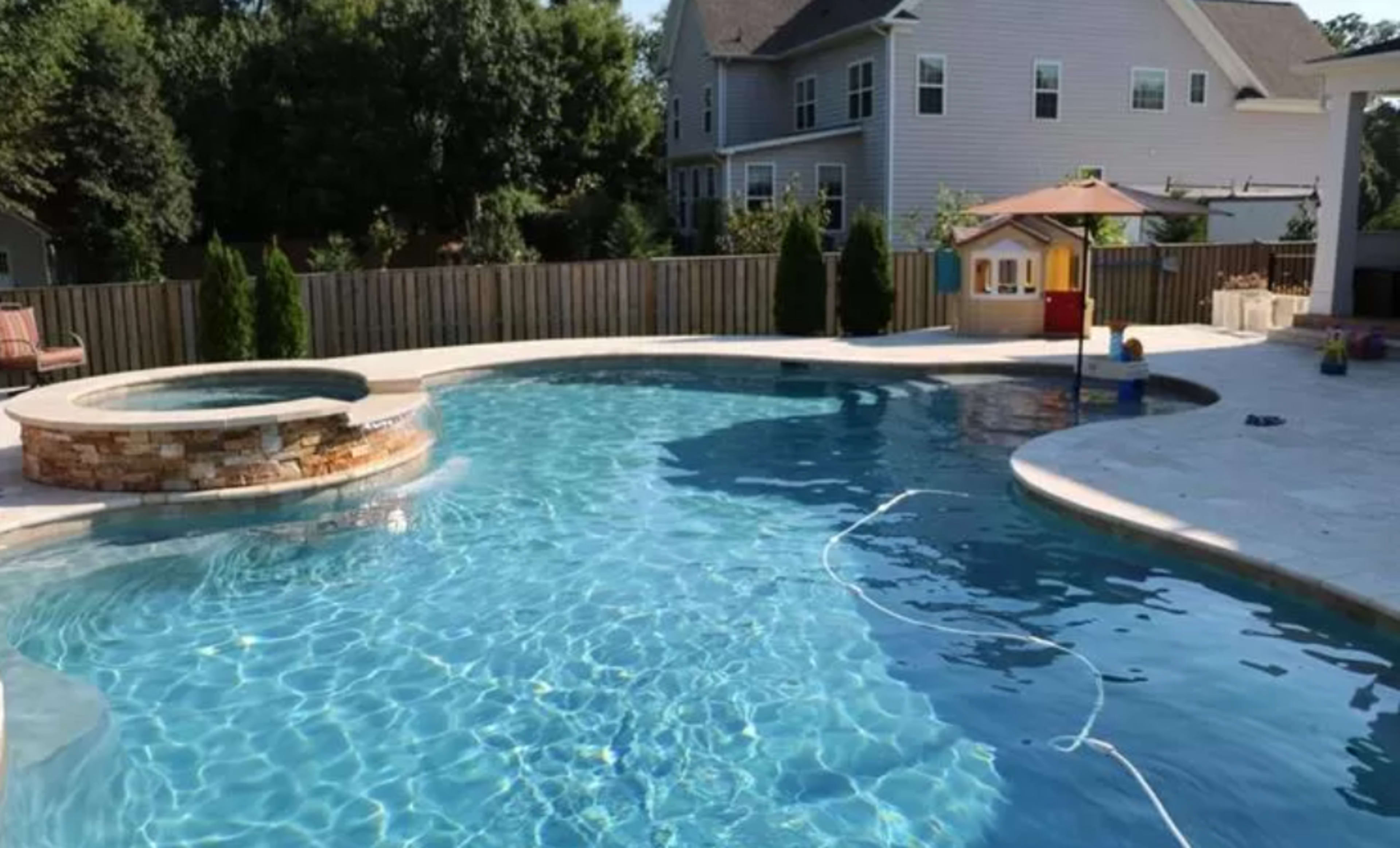 A residential backyard features a swimming pool with a spa area and a children's playhouse visible in the background.
