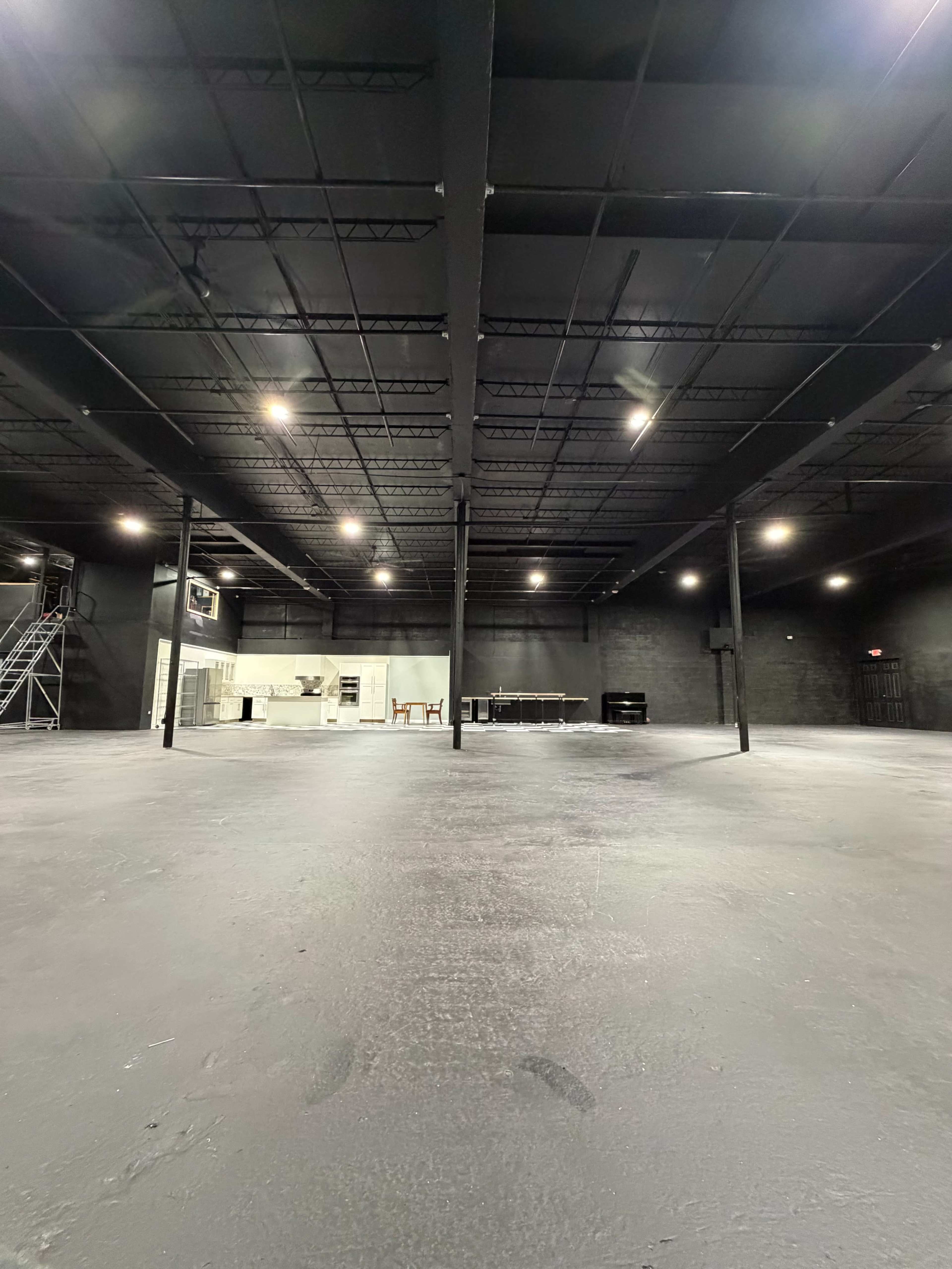 The image shows a large, empty industrial space with black walls and a smooth concrete floor, illuminated by overhead lights.