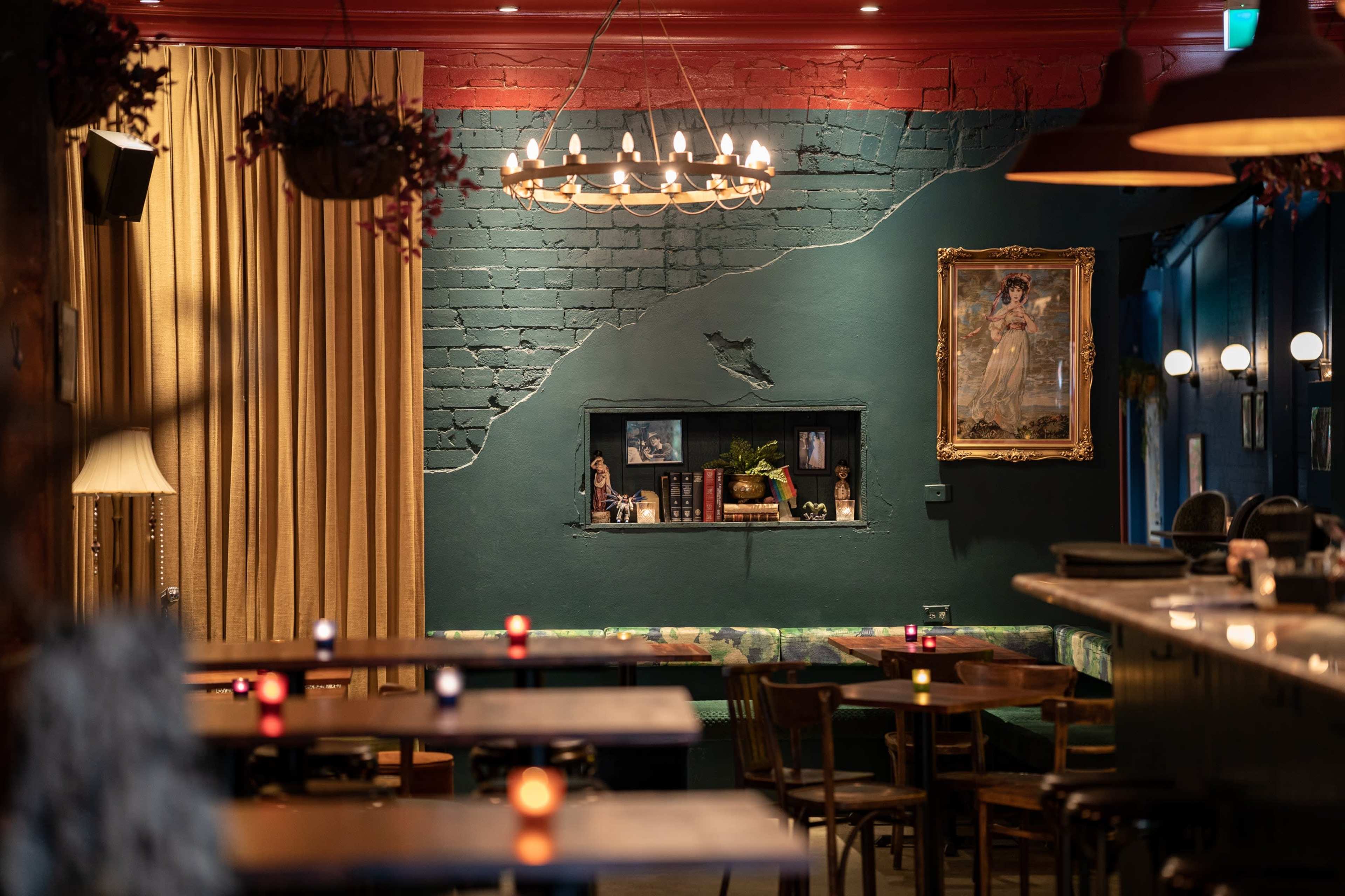 The image shows a dimly lit restaurant with a green accent wall featuring a niche with decorative items, framed artwork, and ambient lighting from table candles.