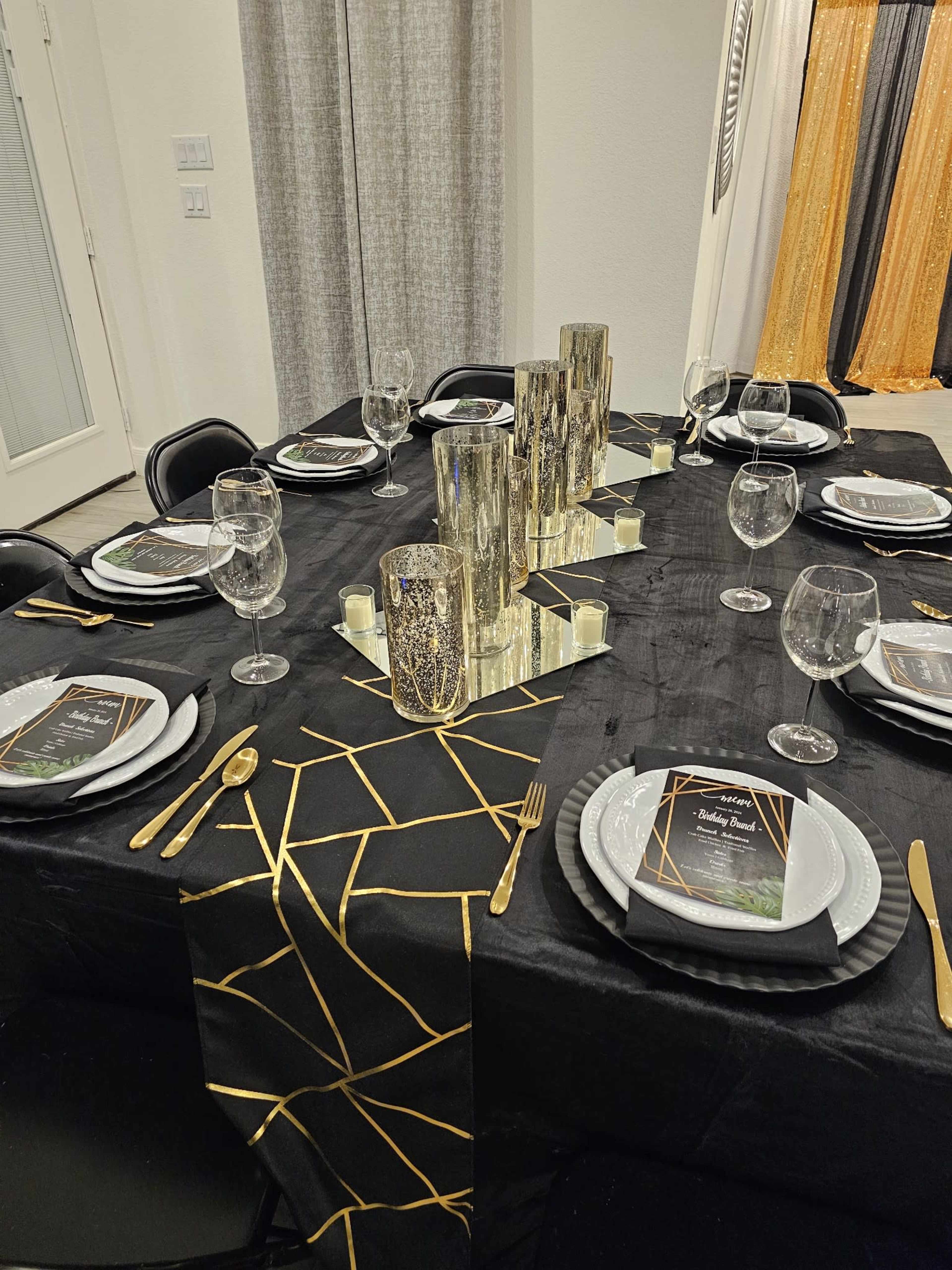 A dining table is elegantly set with black tableware, gold accents, and reflective centerpieces.