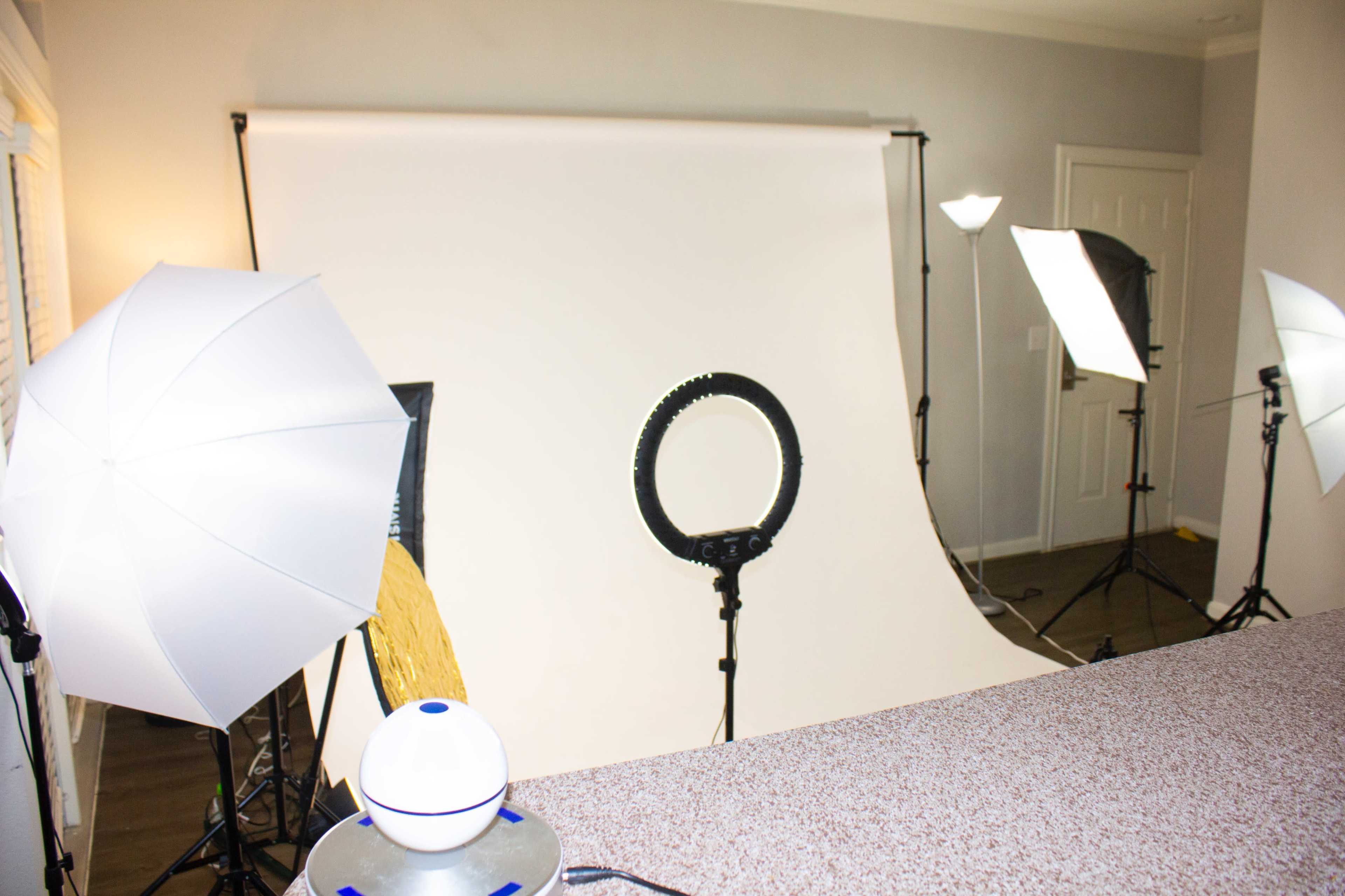 A photography studio setup with a white backdrop and various lighting equipment, including softboxes and a ring light.