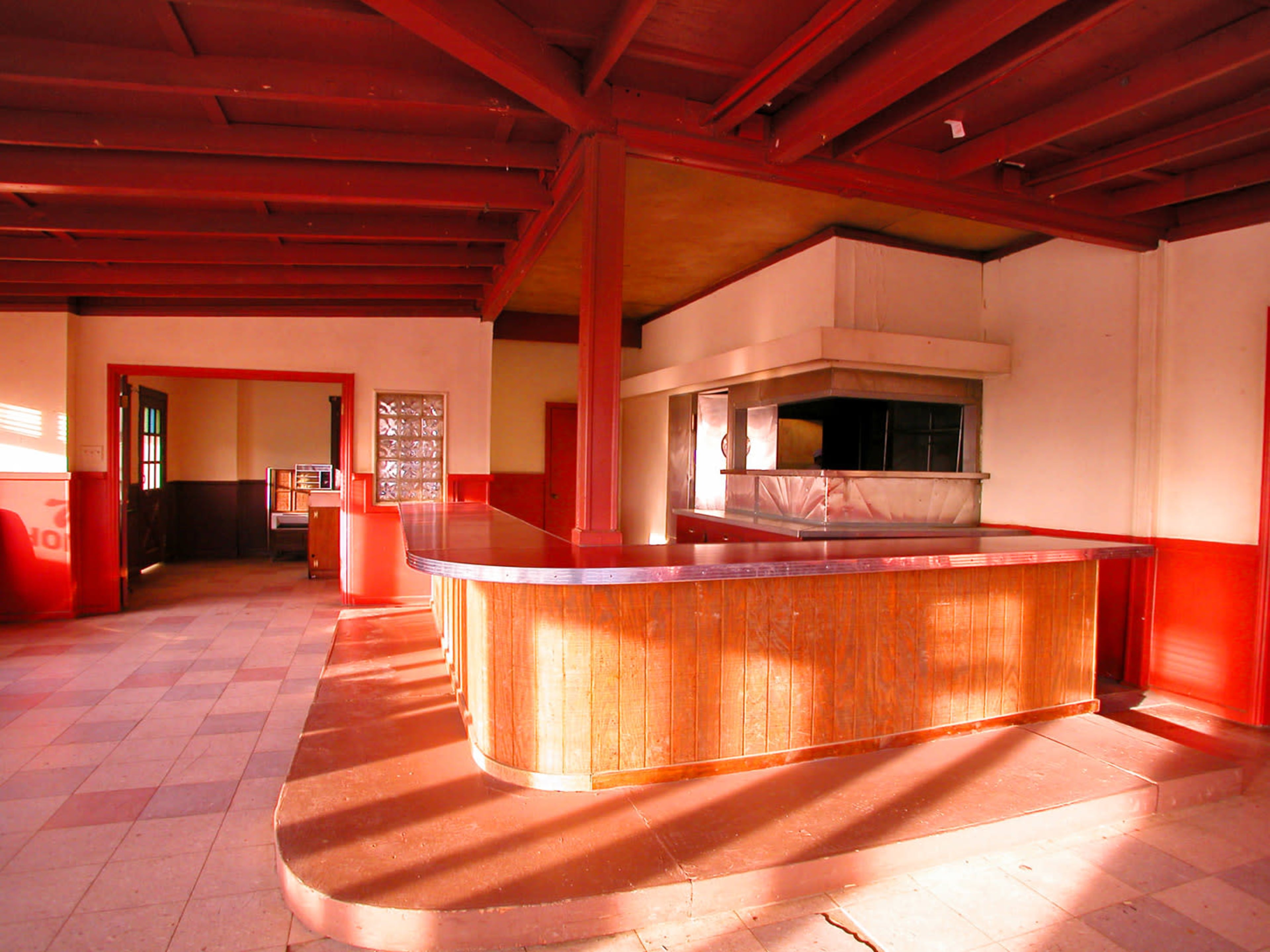 The image shows an empty, well-lit interior of a building featuring a wooden counter and red walls.