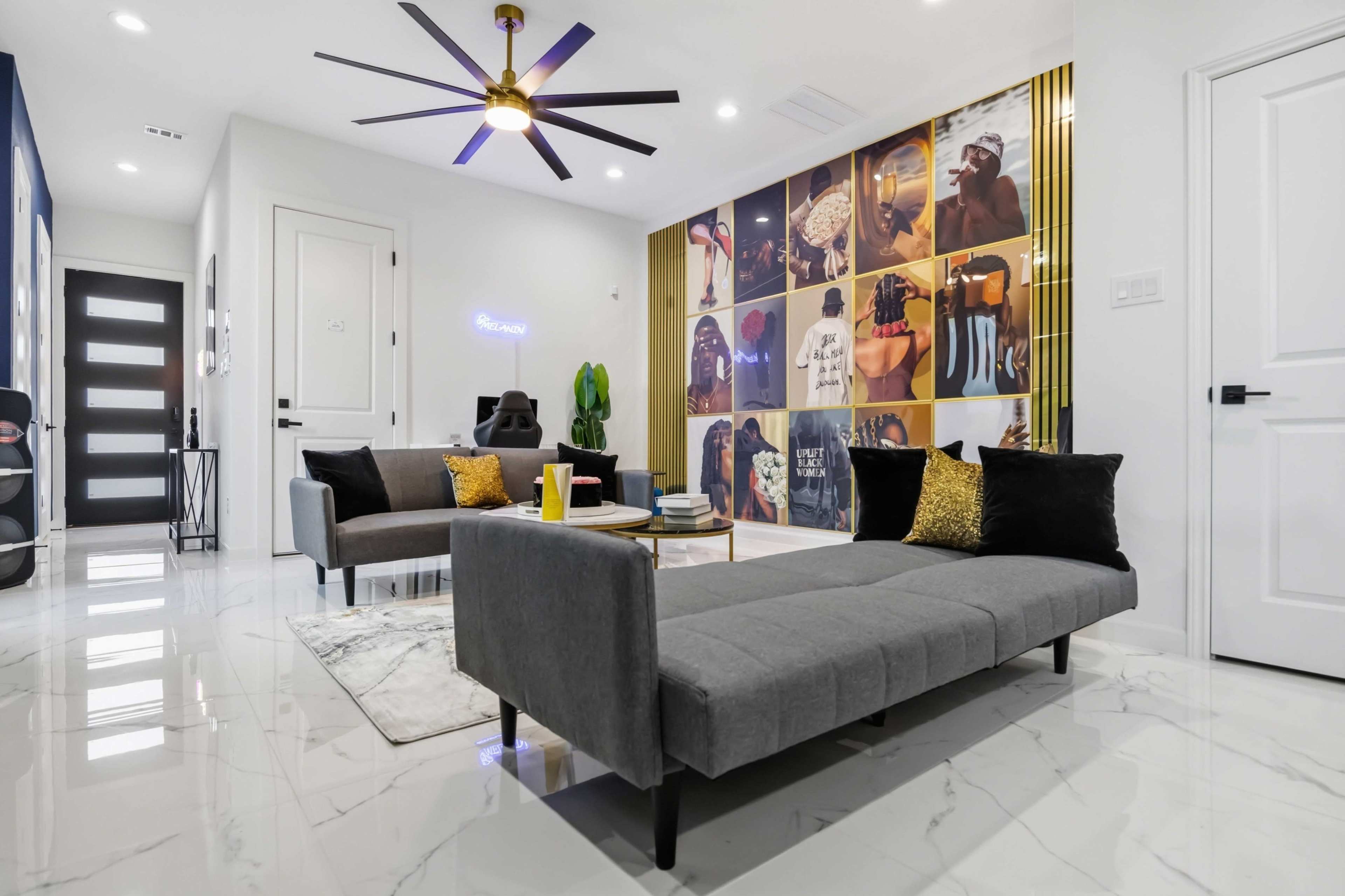 The image shows a modern living room with a gray sectional sofa, a coffee table, a gallery wall featuring a collage of photographs, and a stylish ceiling fan.