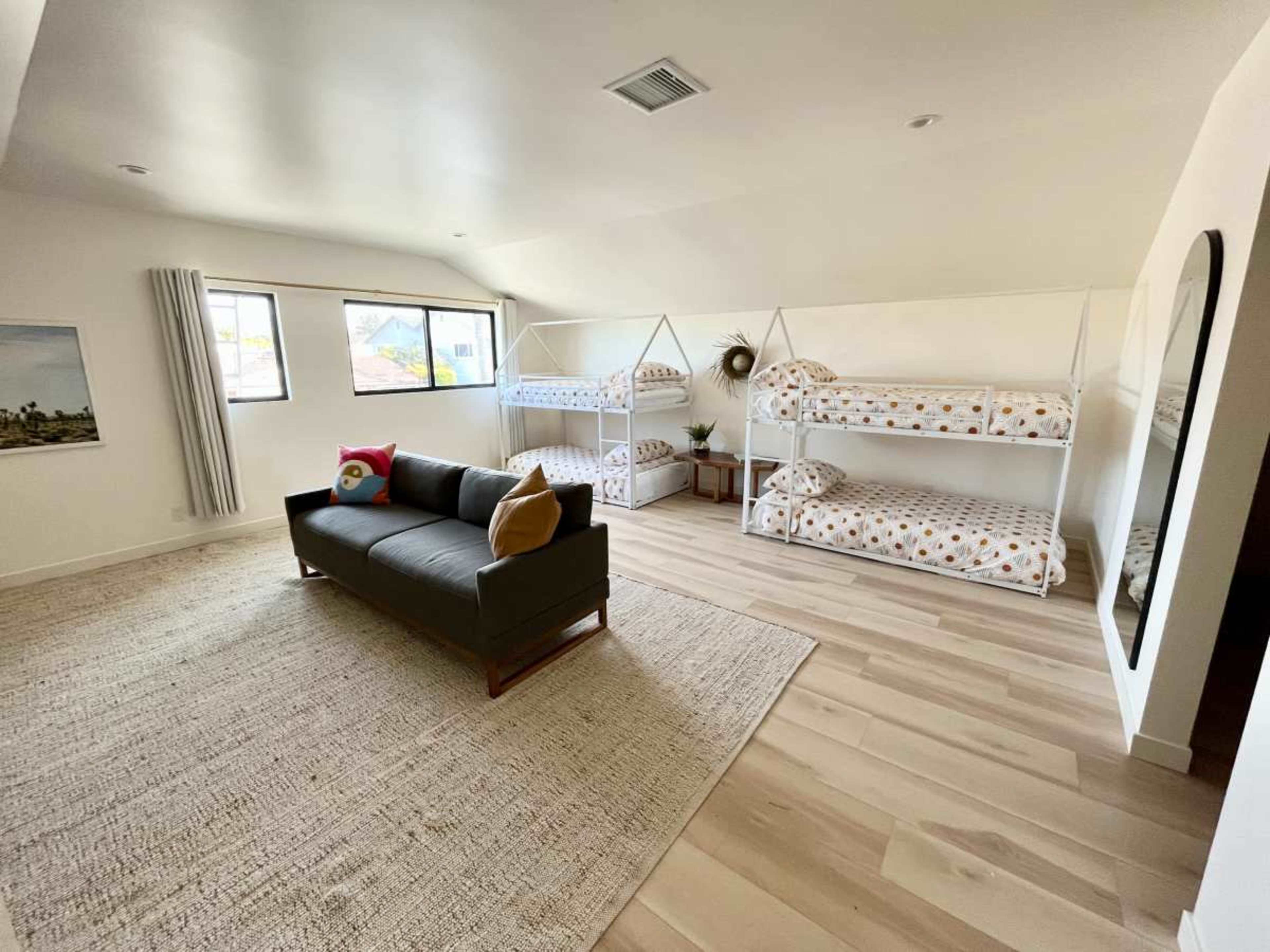 The room features two sets of metal frame bunk beds and a gray sofa arranged on a light wood floor.