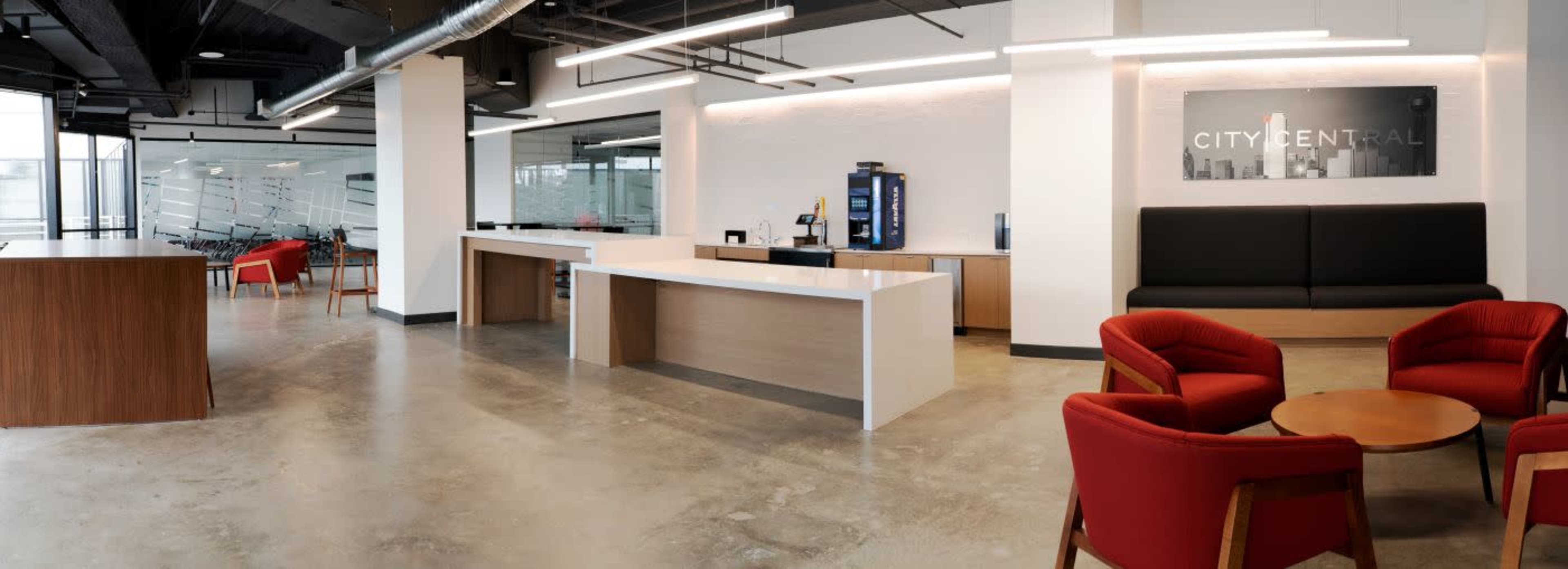 The image shows a modern office reception area with sleek furniture, a coffee station, and large windows allowing natural light.
