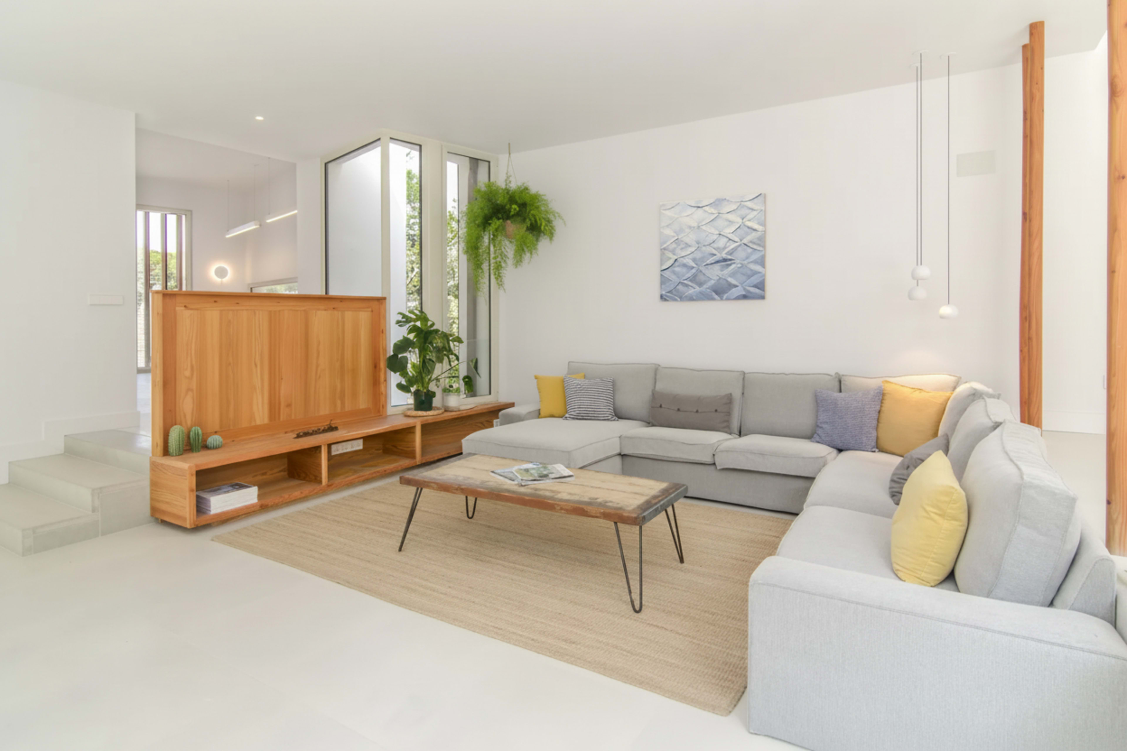 The image shows a modern, well-lit living room with a large sectional sofa, a wooden coffee table, and a decorative indoor plant.