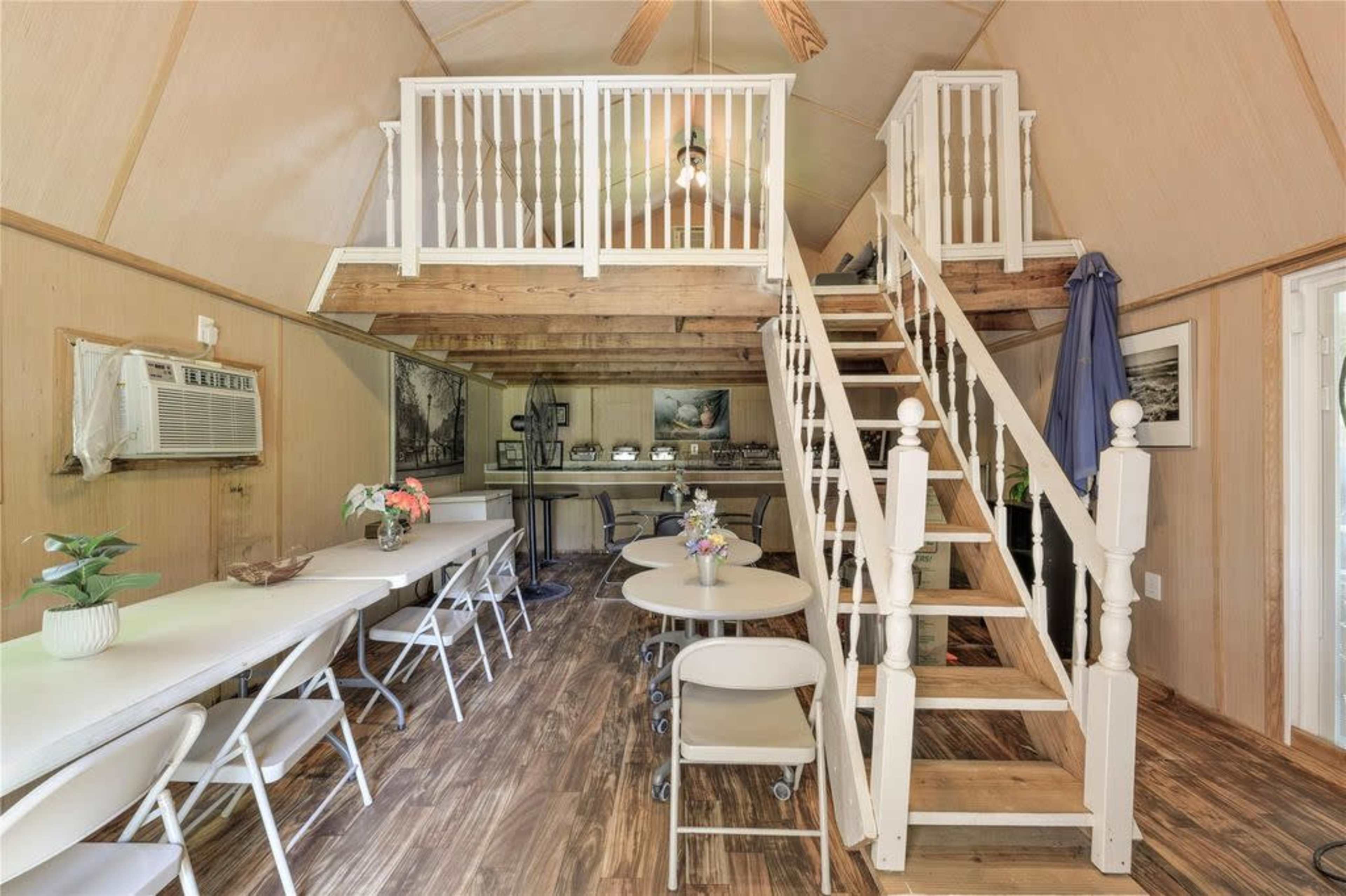 The interior features a spacious, two-story room with a loft and a dining area furnished with white tables and chairs.